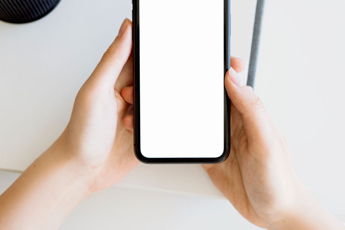 Two hands holding a smartphone with a blank white screen against a plain light background