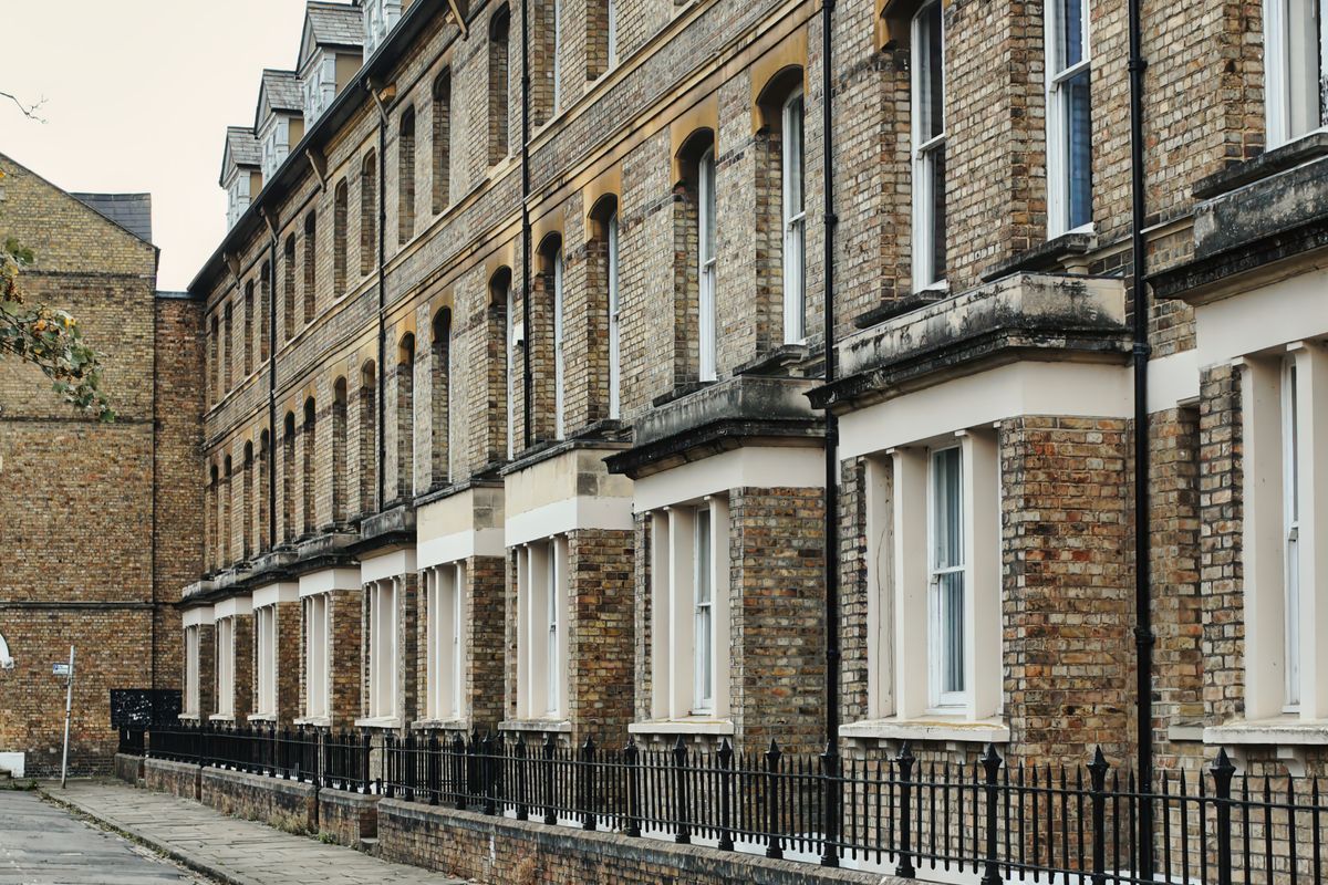 Long terrace of Victorian yellow brick houses with white bay windows behind black iron railings