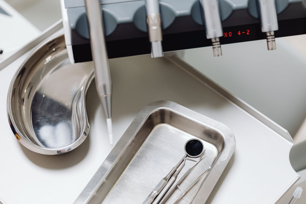 Dental mirror and instruments on a steel tray beside a kidney dish, with handpieces hanging from the dental unit above