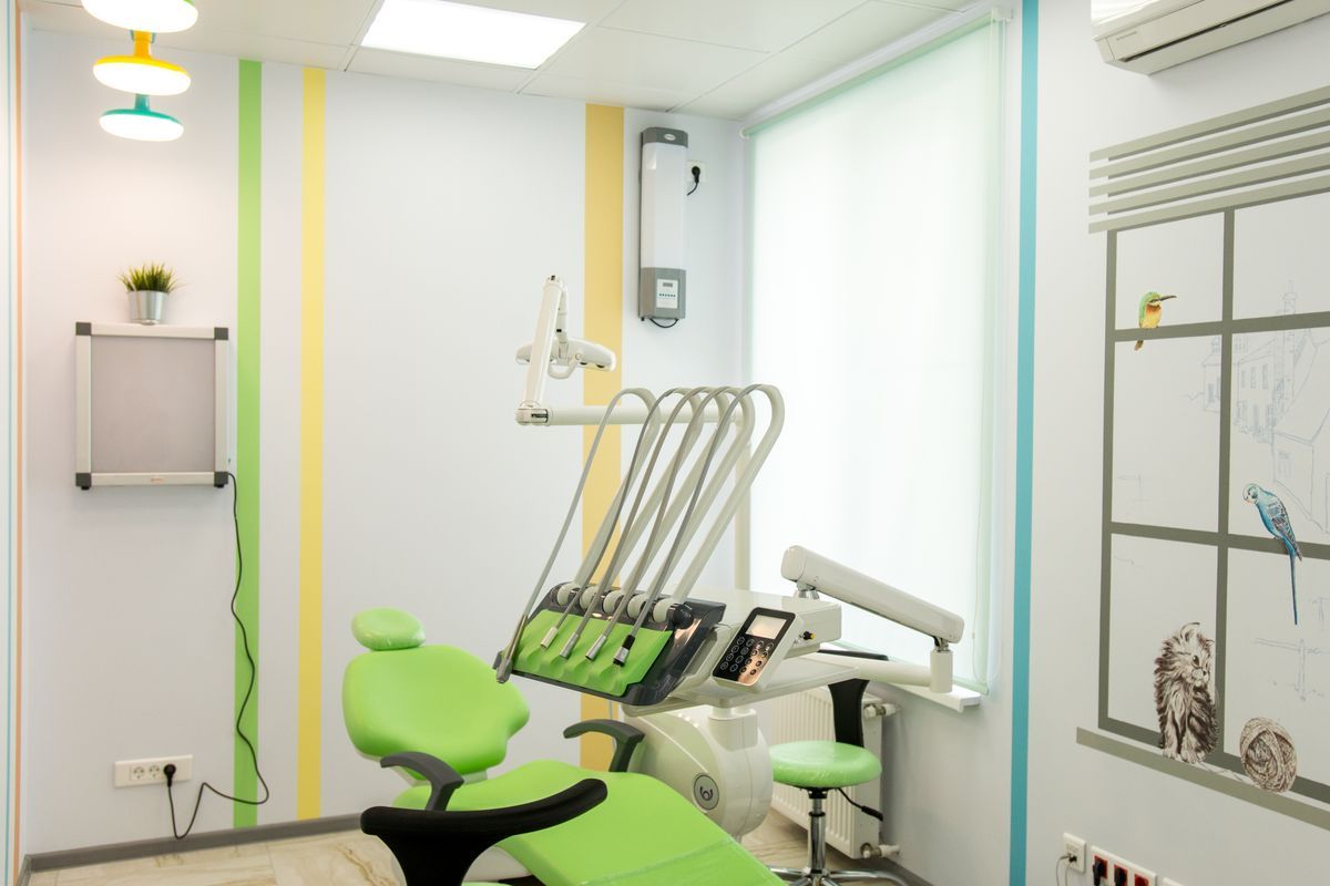 Dental surgery with a lime green treatment chair, striped yellow and green wall and a white wall unit by a frosted window
