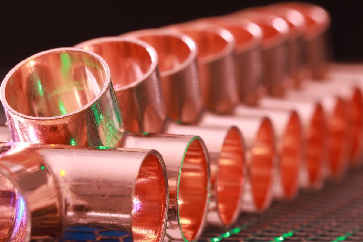 Rows of copper pipe fittings lined up on a metal mesh surface