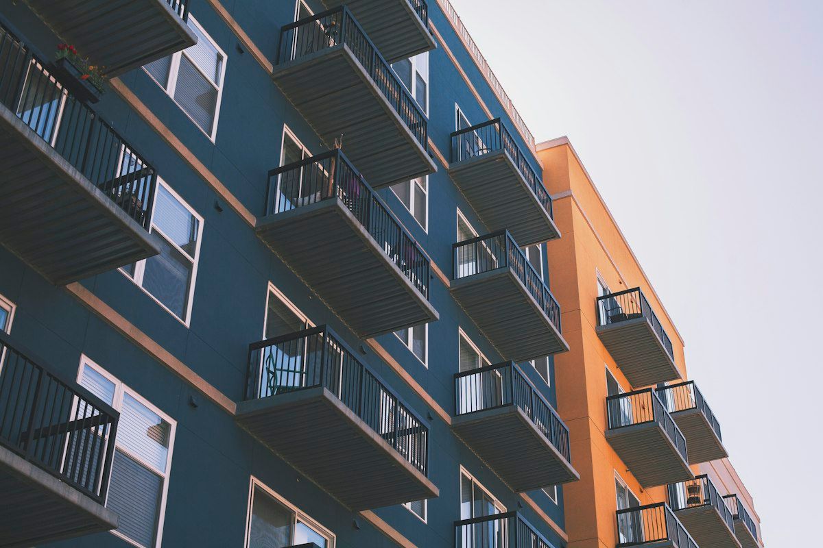 Blue and orange apartment block with metal balconies, seen from below