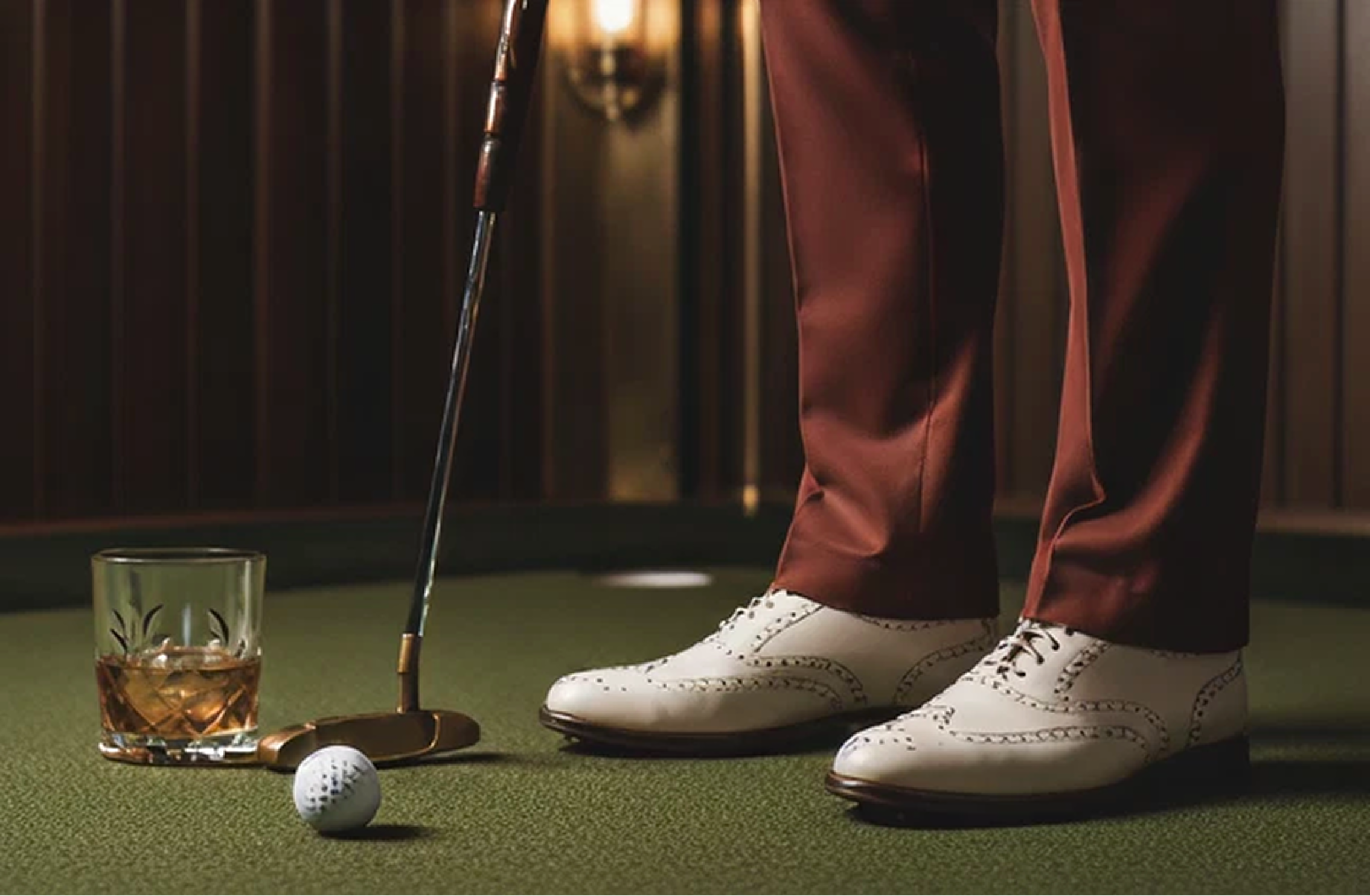Whiskey, a putter, and wingtips on the green at The Backswing