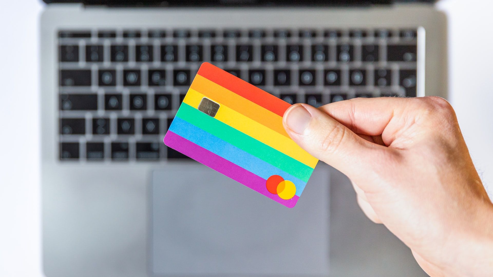 Image of an hand that holds a rainbow-coloured MasterCard with two fingers