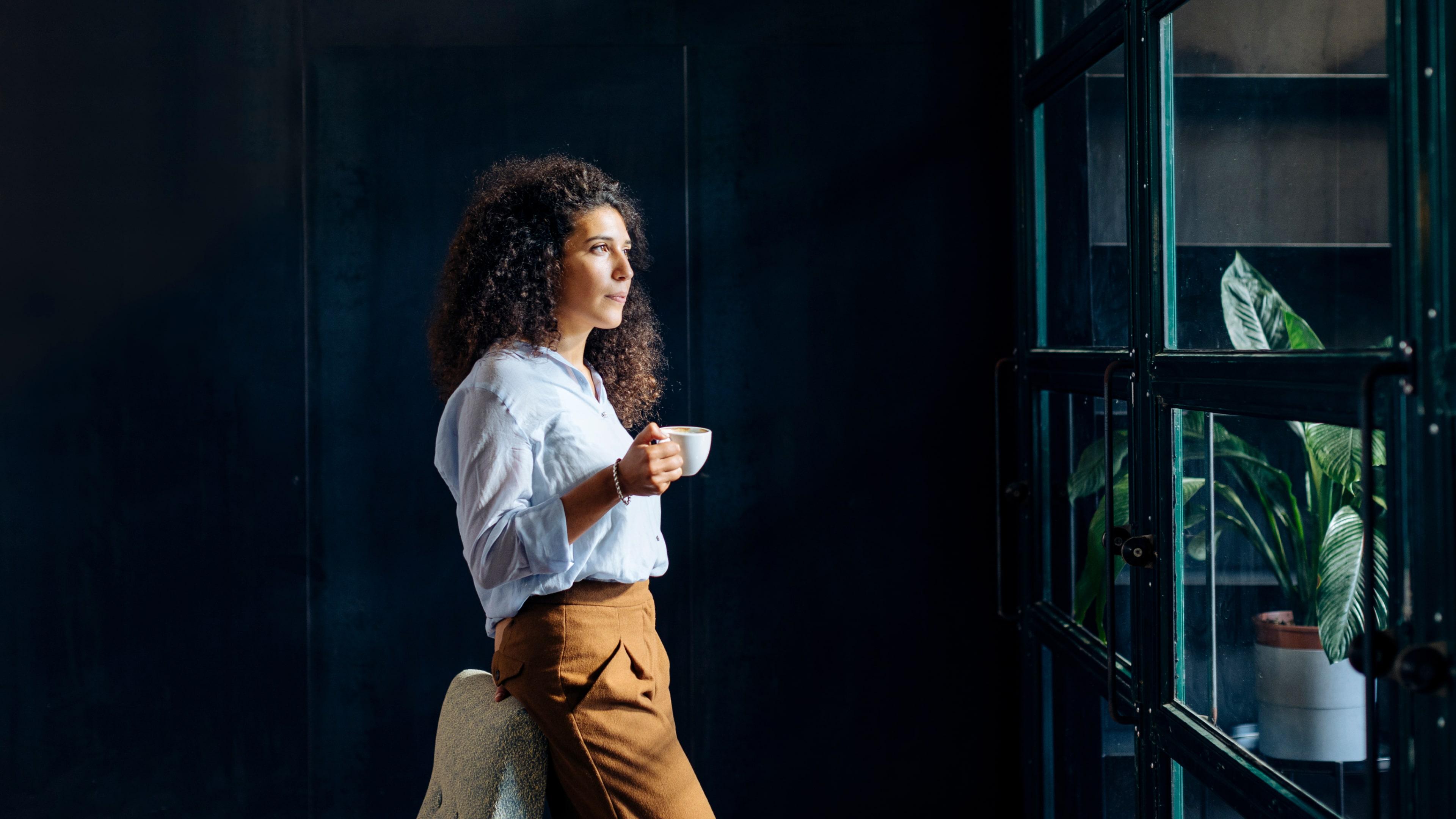 A curly girl drinking coffee while watching outside a window
