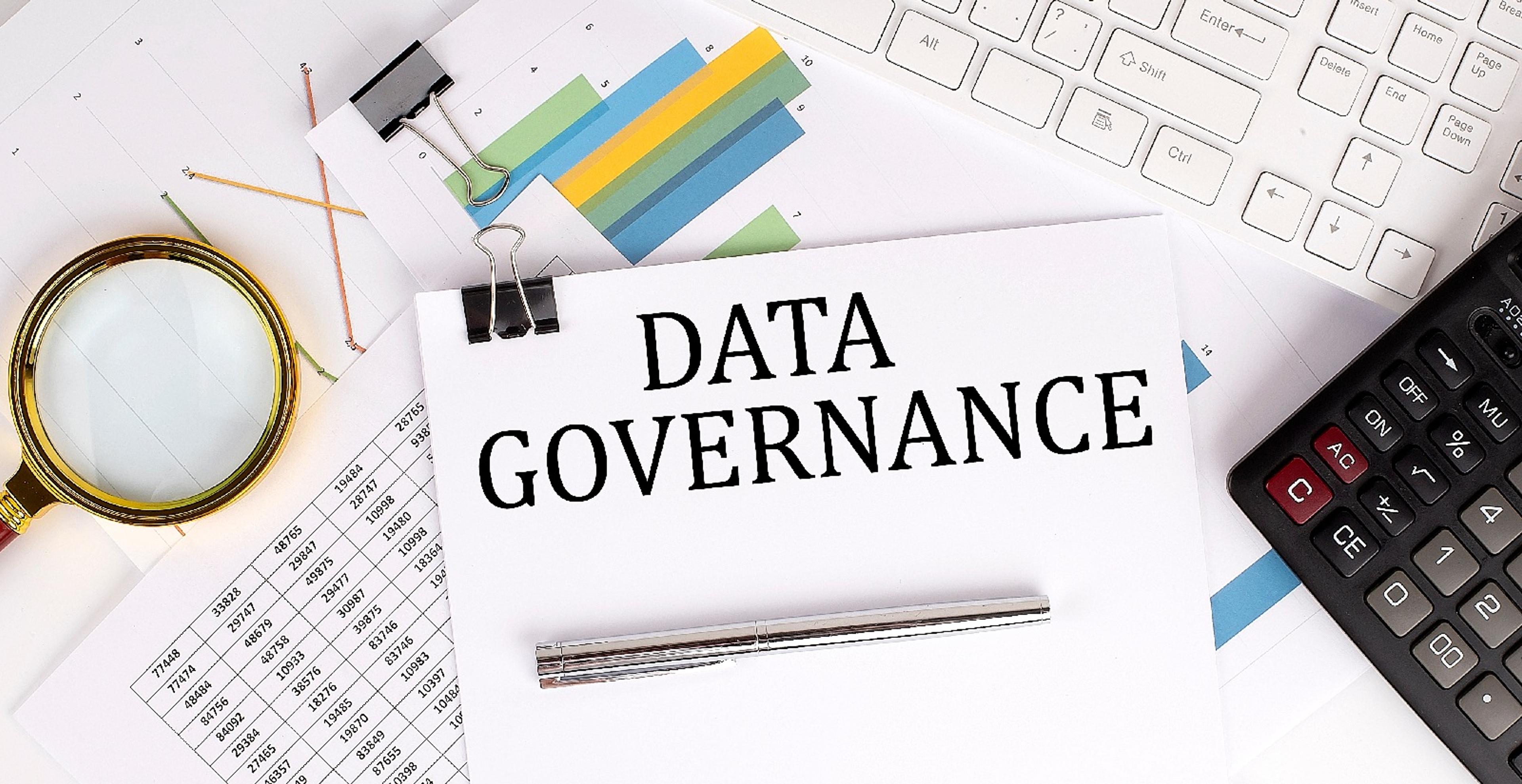 Paper labeled ‘Data Governance’ with charts, calculator, keyboard, pen, and magnifying glass.
