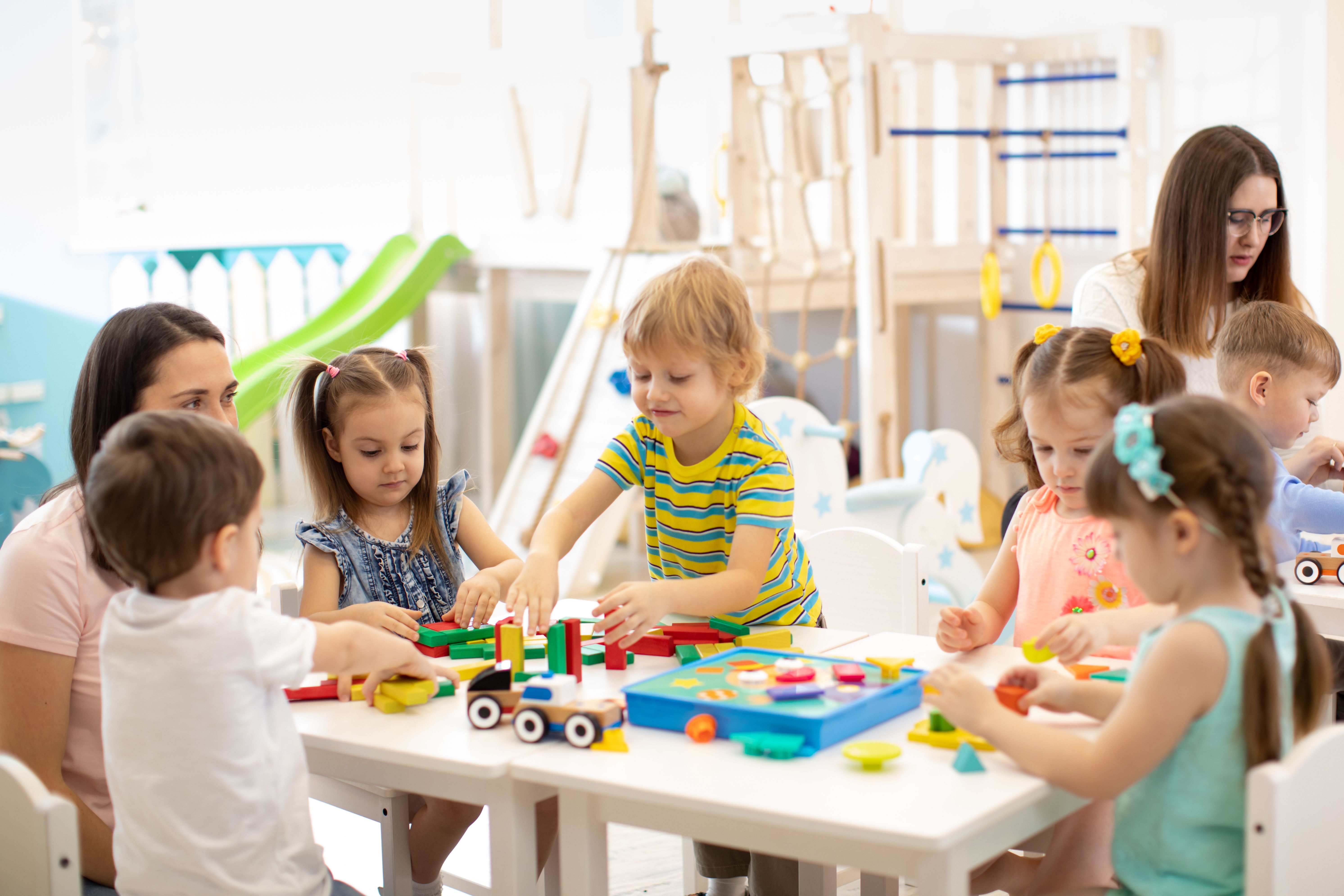Children playing together with toys in a preschool classroom while educators supervise.