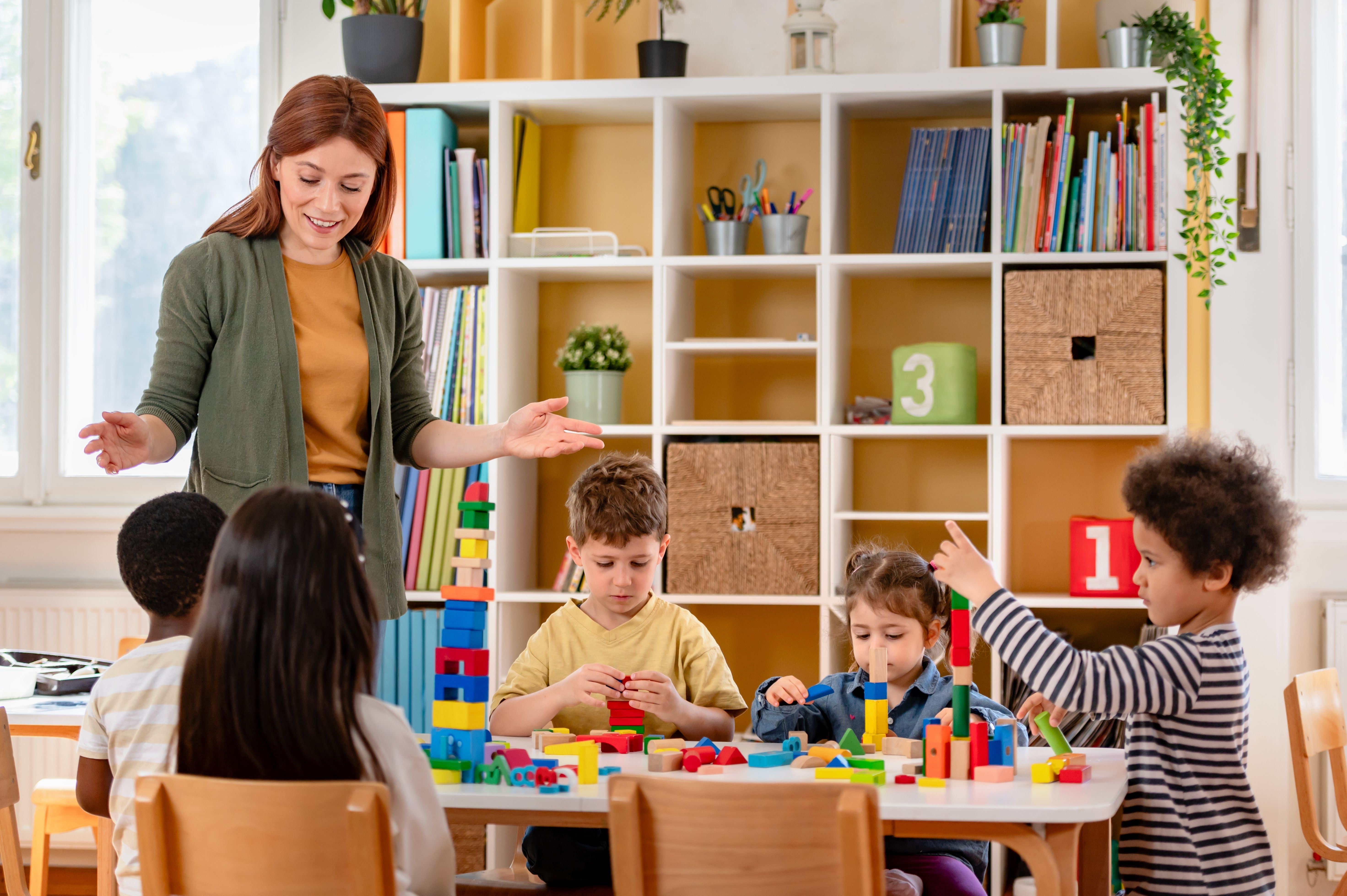 Educator supporting a group of children playing with building blocks in a childcare classroom.