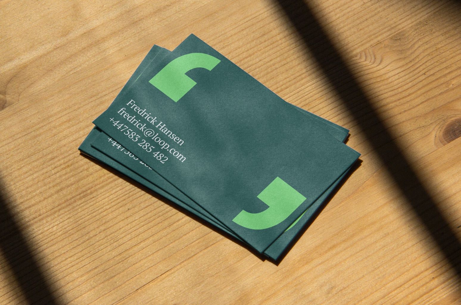 Stack of green Loop business cards on wooden table.