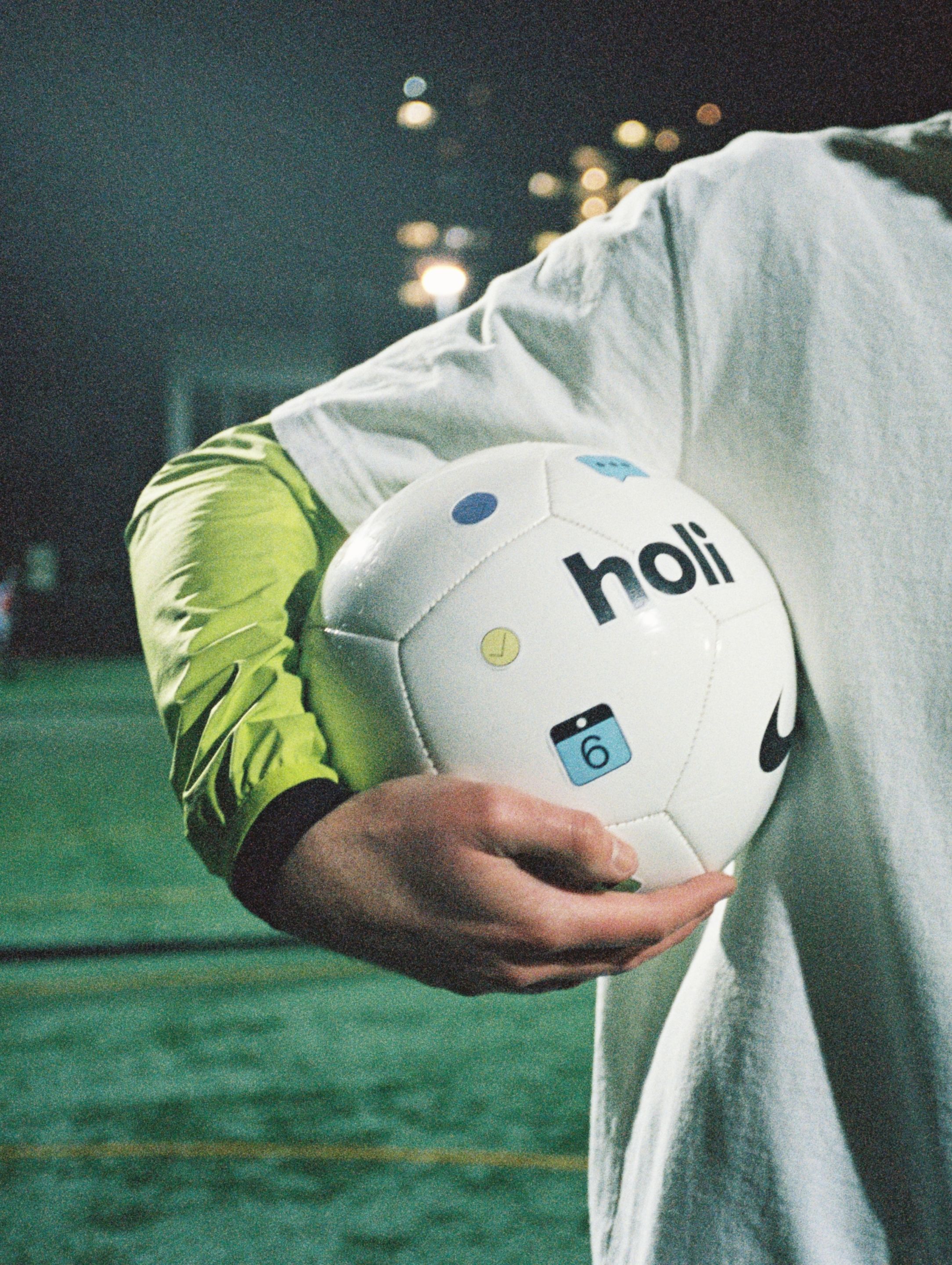 A person standing on a football pitch holding a football covered in holi stickers 
