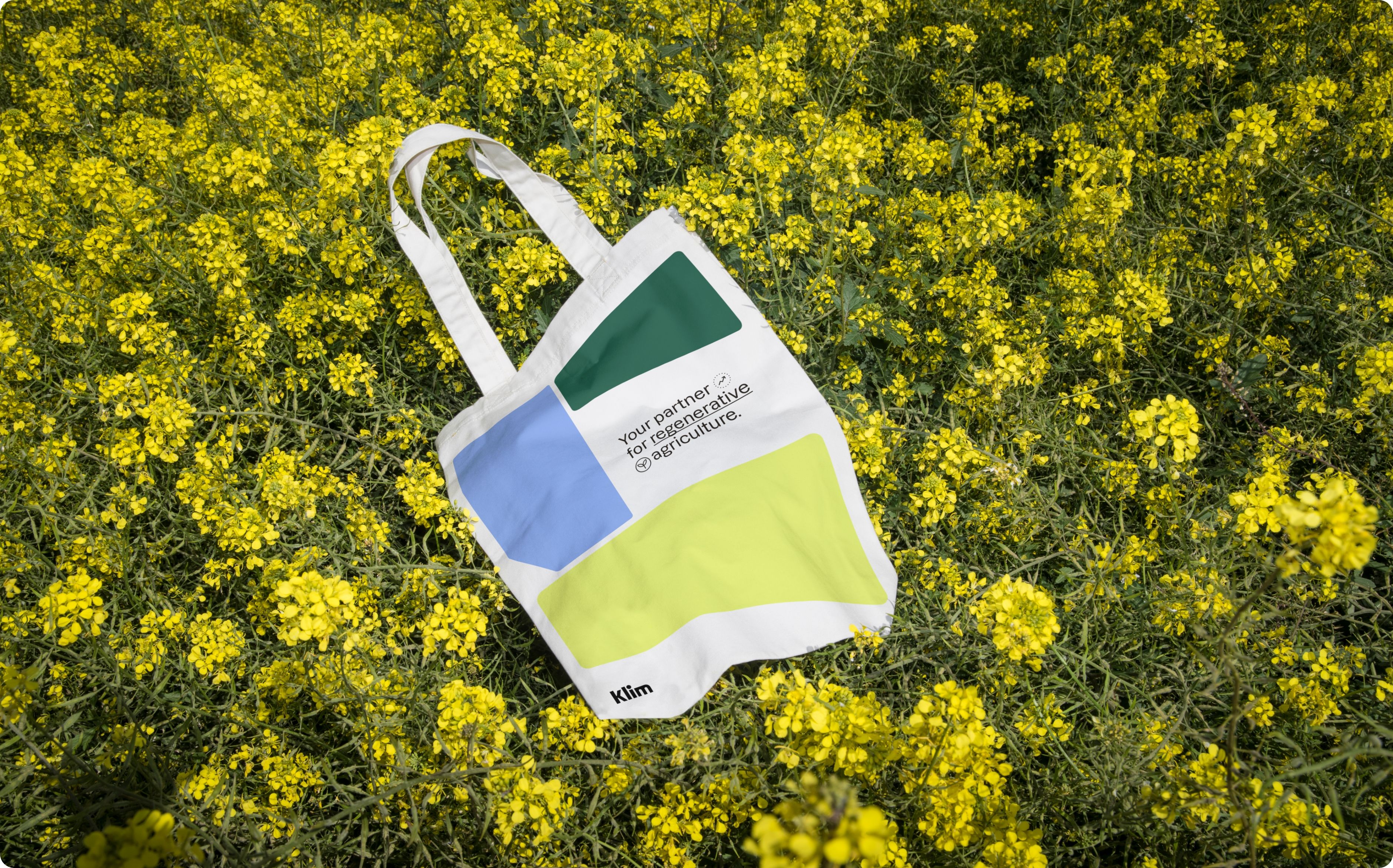 Klim branded tote bag lying on a field of rapeseed.
