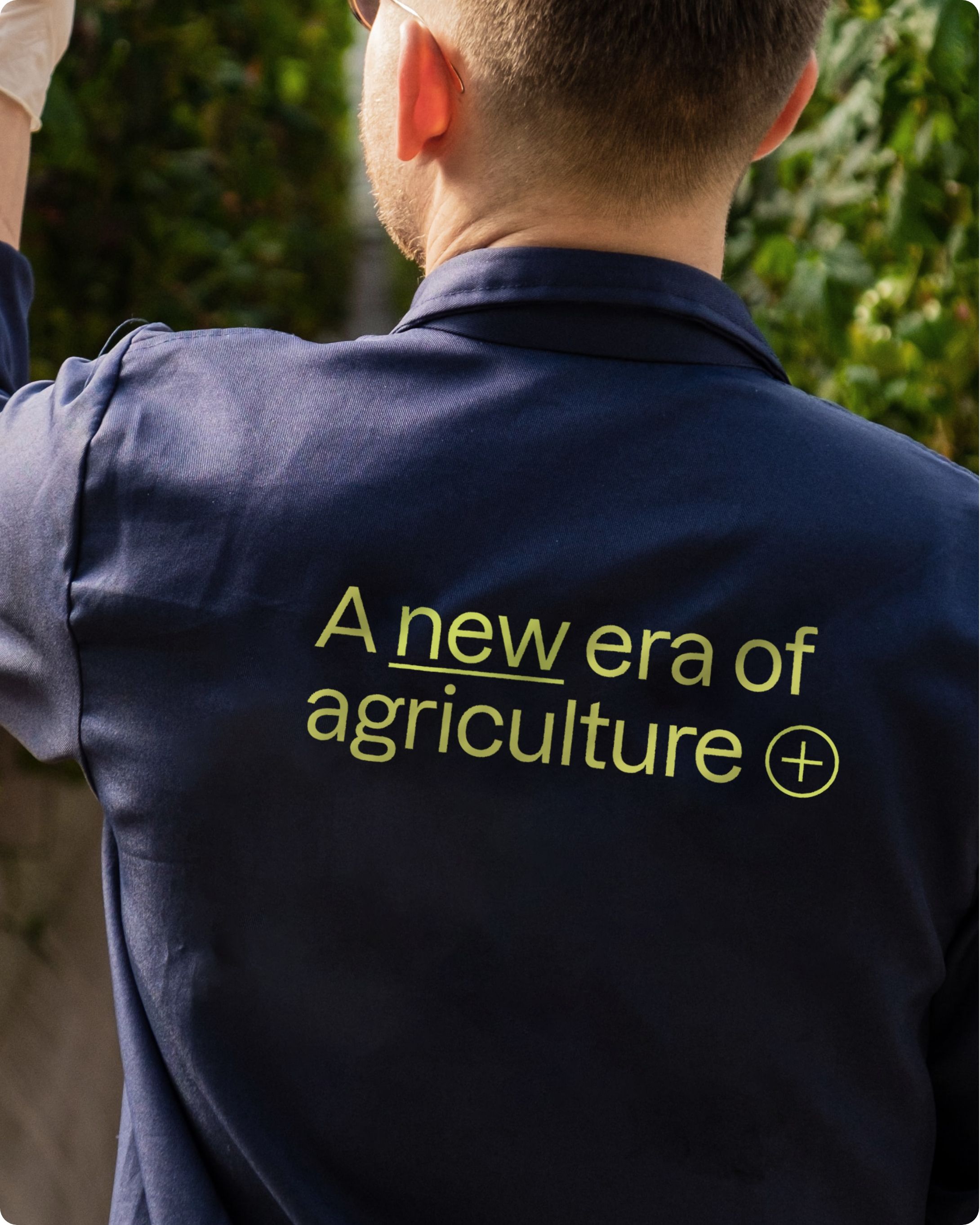 The back of a farmer wearing a blue jacket reading 'A new era of agriculture'.