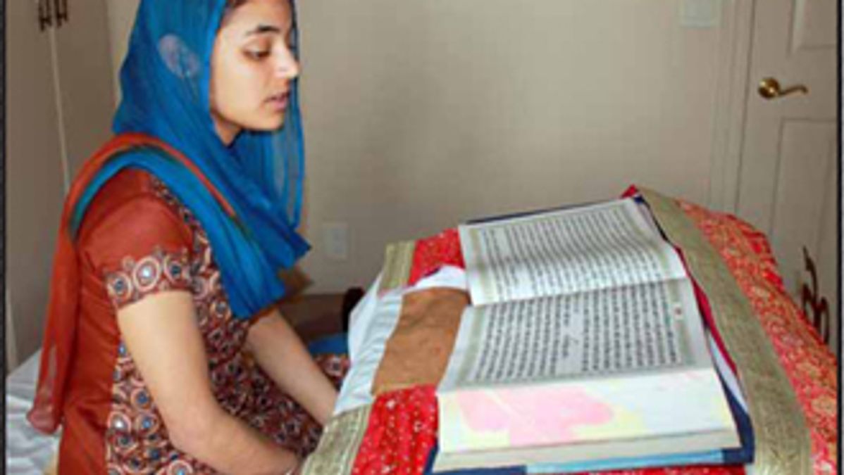 Sikh woman reading Siri Guru Granth Sahib in her home