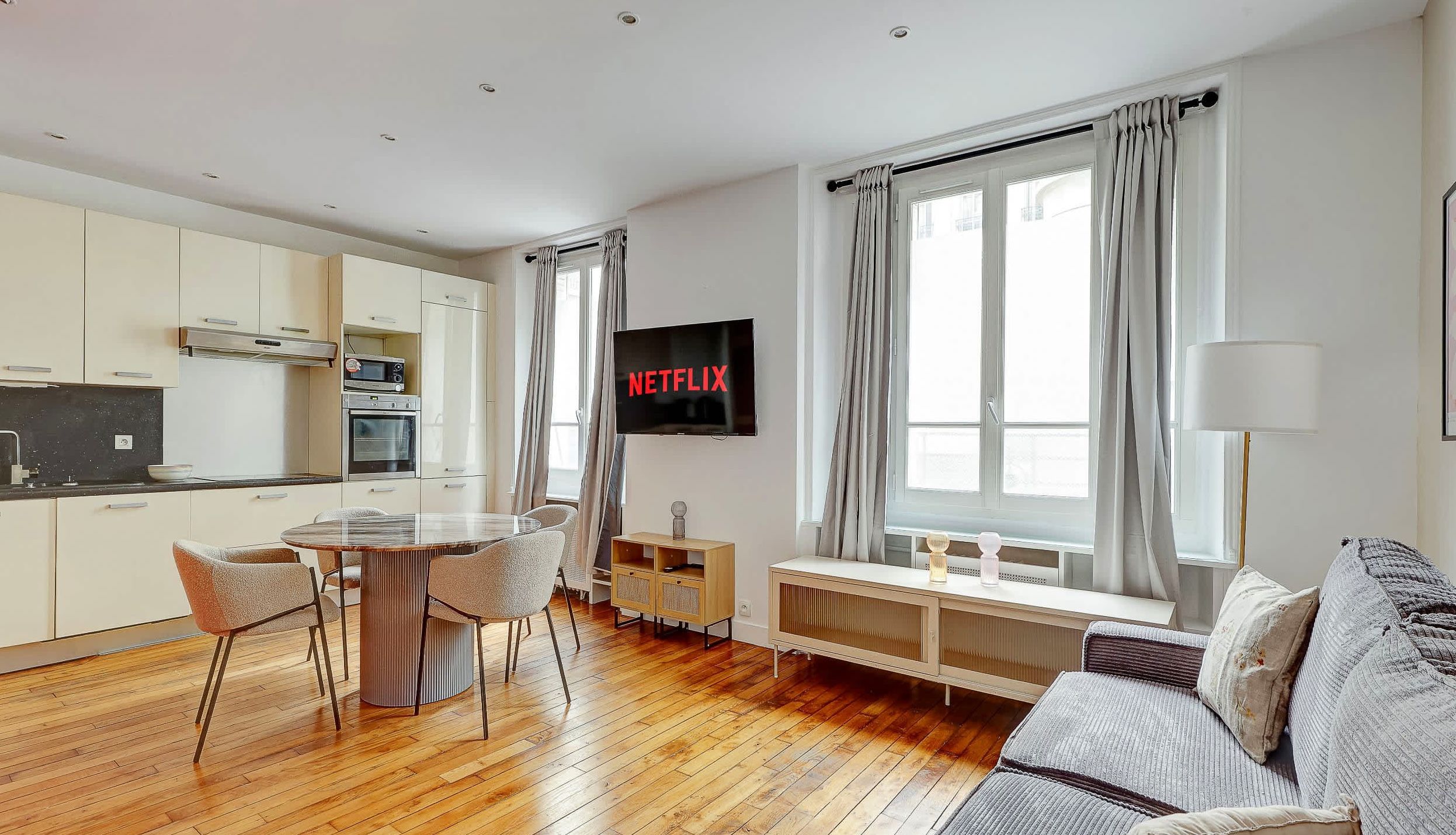 Modern Montparnasse apartment living room with convertible sofa, dining corner, and bright natural light.