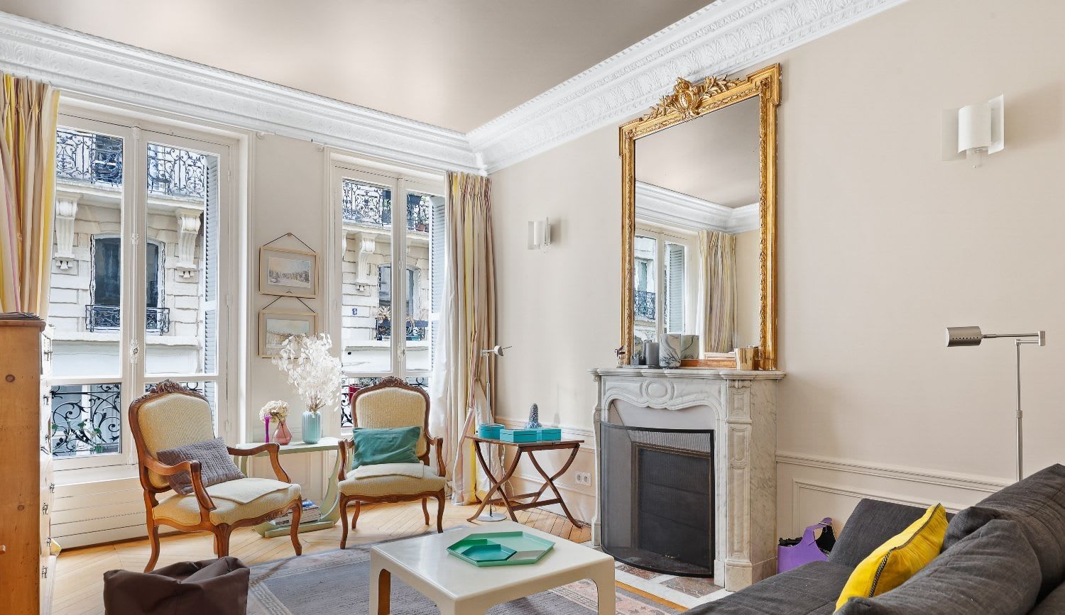 Salle à manger haussmannienne d'un appartement meublé rue Lentonnet Paris 9e, suspension Vertigo au-dessus d'une table ovale et chaises Louis Ghost sous des moulures d'époque