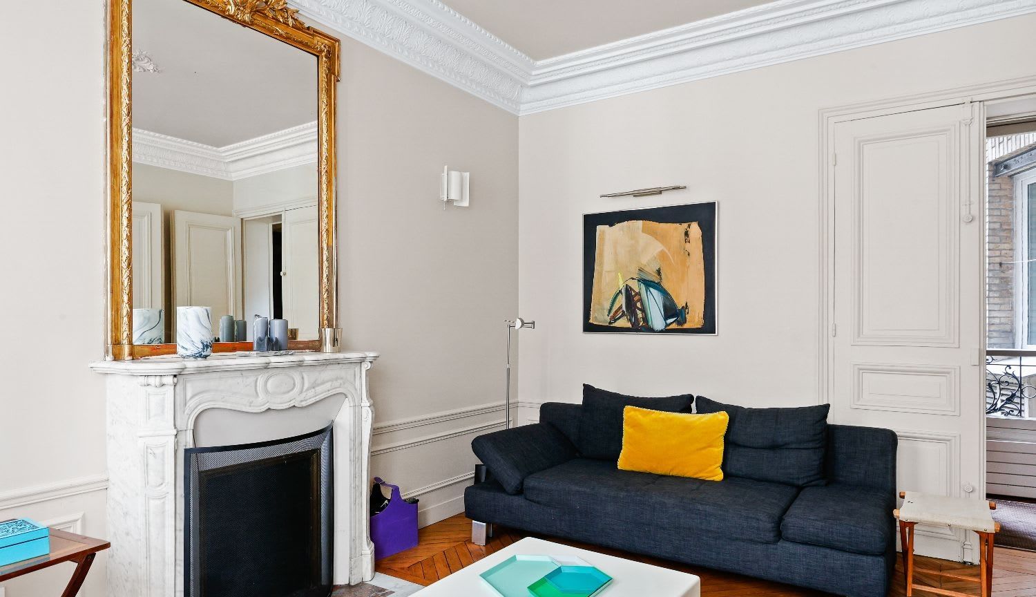 Salle à manger haussmannienne d'un appartement meublé rue Lentonnet Paris 9e, suspension Vertigo au-dessus d'une table ovale et chaises Louis Ghost sous des moulures d'époque
