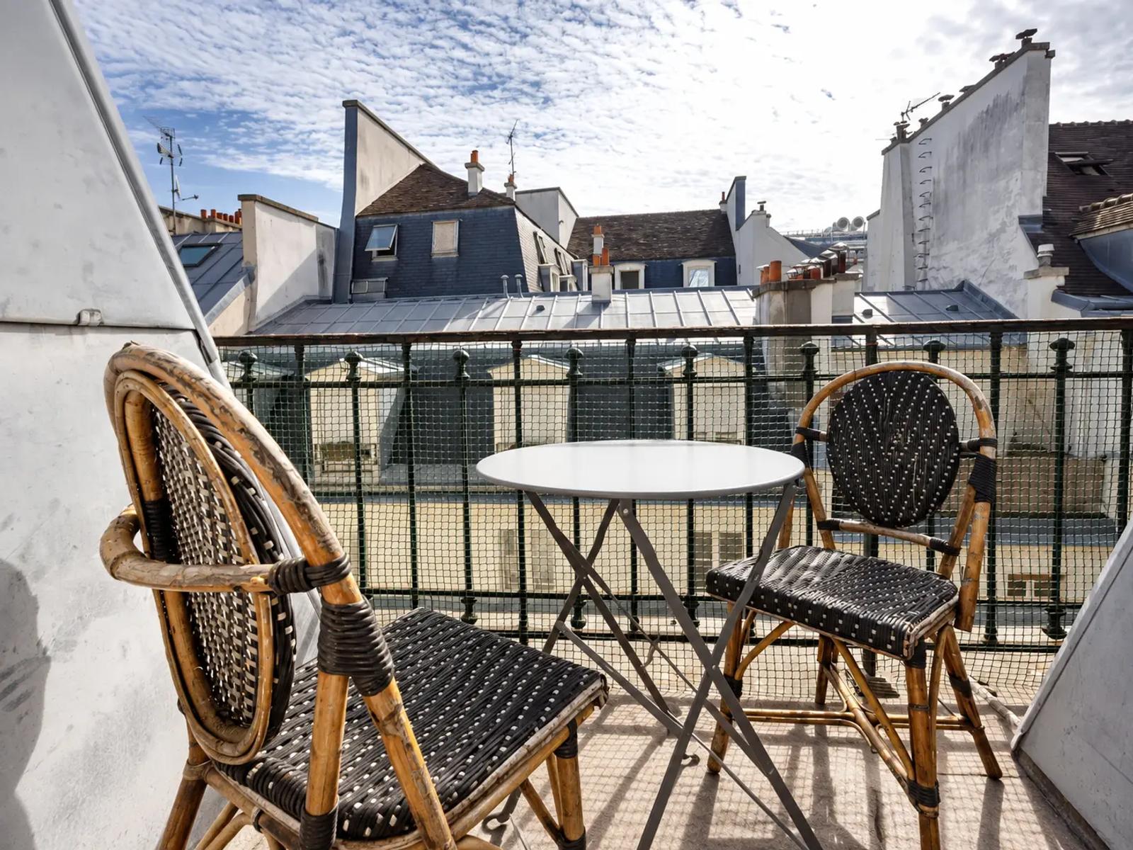 Balcon avec table de bistrot et vue sur les toits de Paris