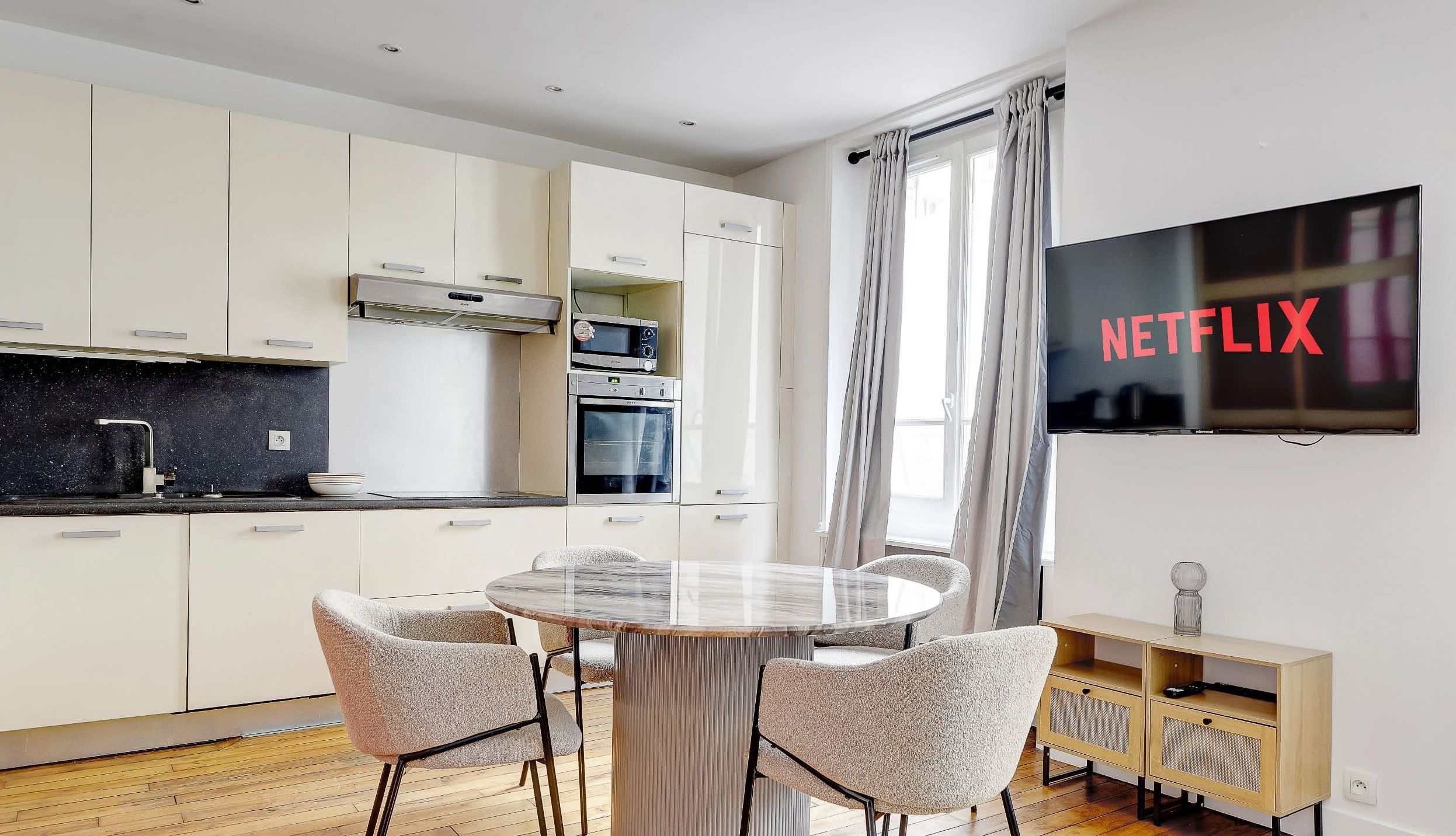 Modern Montparnasse apartment living room with convertible sofa, dining corner, and bright natural light.