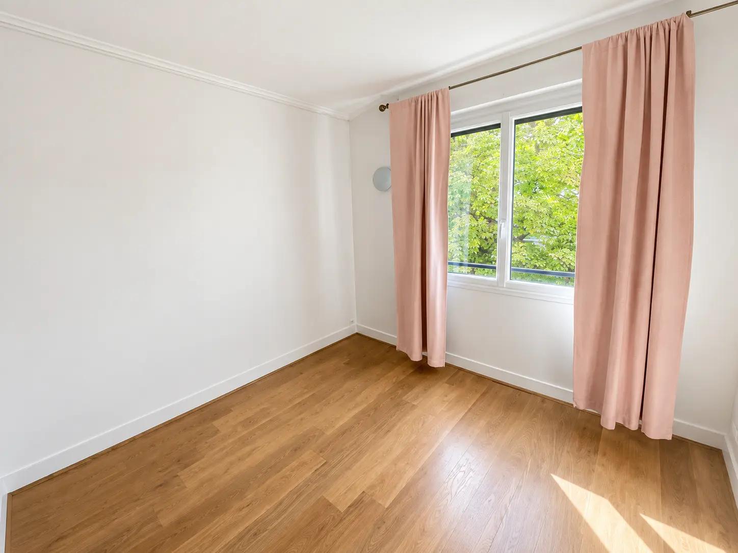 Bedroom with wooden floors, pink curtains and leafy outlook