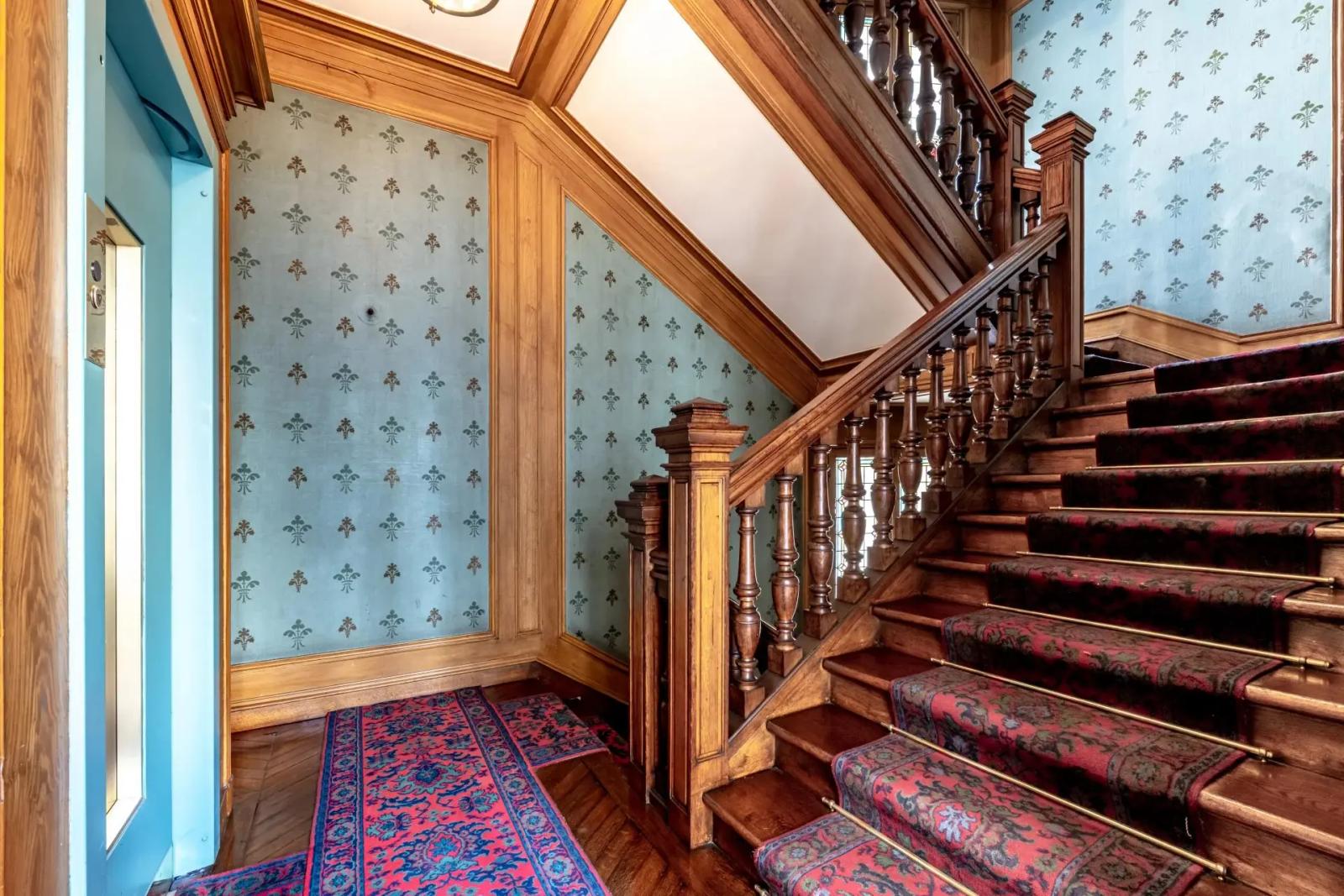 Escalier en bois avec tapis à motifs près de l’ascenseur