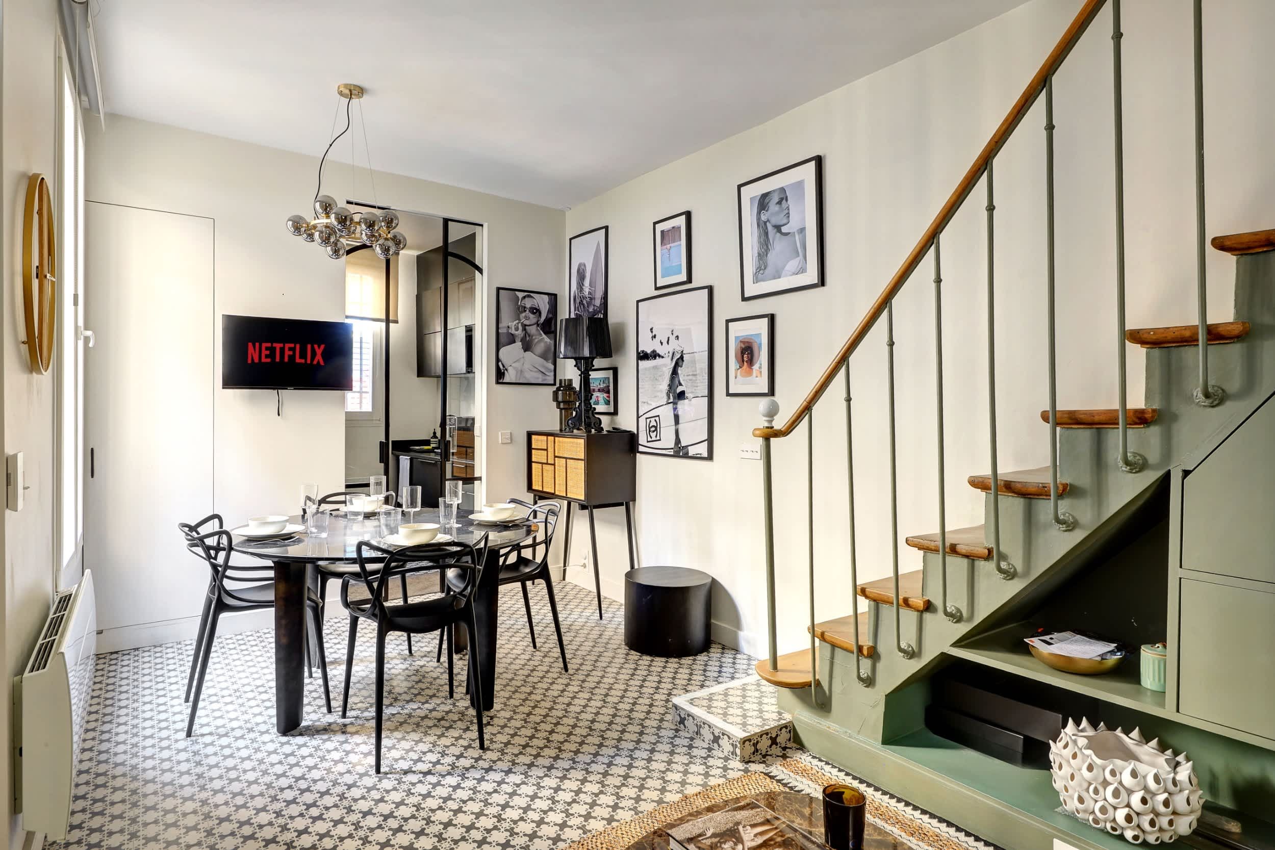 Canapé convertible en lit et coin repas, dans un espace moderne et lumineux avec escalier.