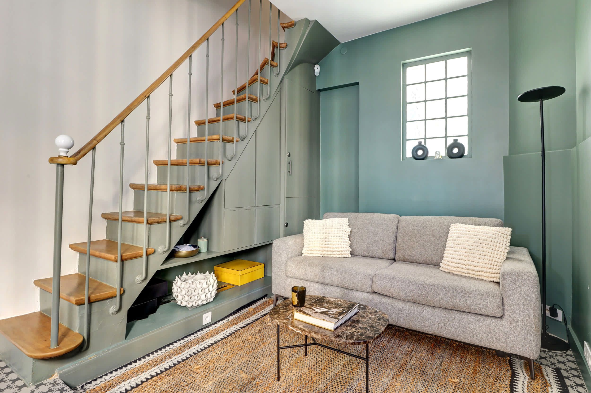 Canapé convertible en lit et coin repas, dans un espace moderne et lumineux avec escalier.