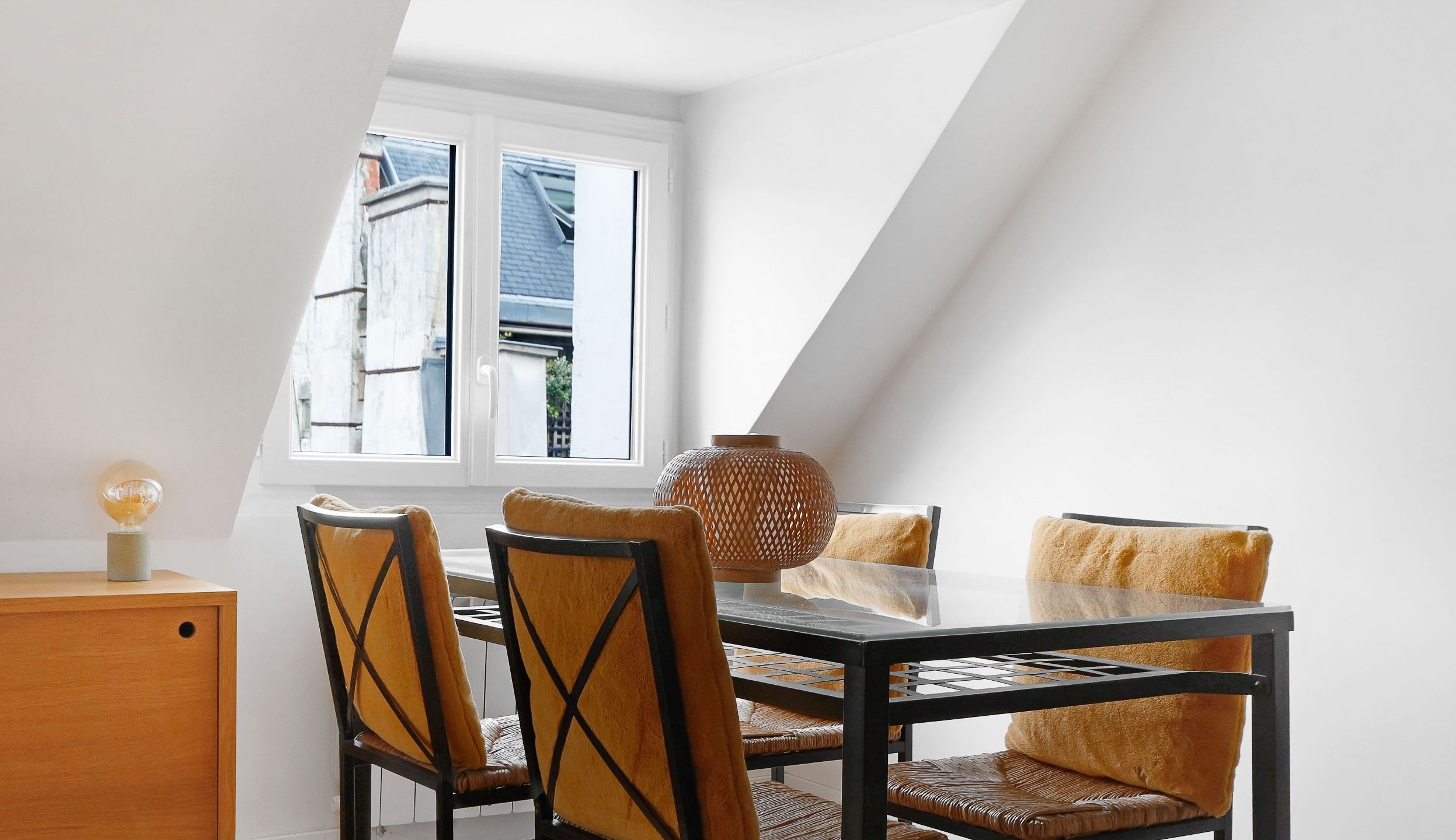 Séjour lumineux sous les toits avec poutres apparentes, coin repas avec une table et des chaises.