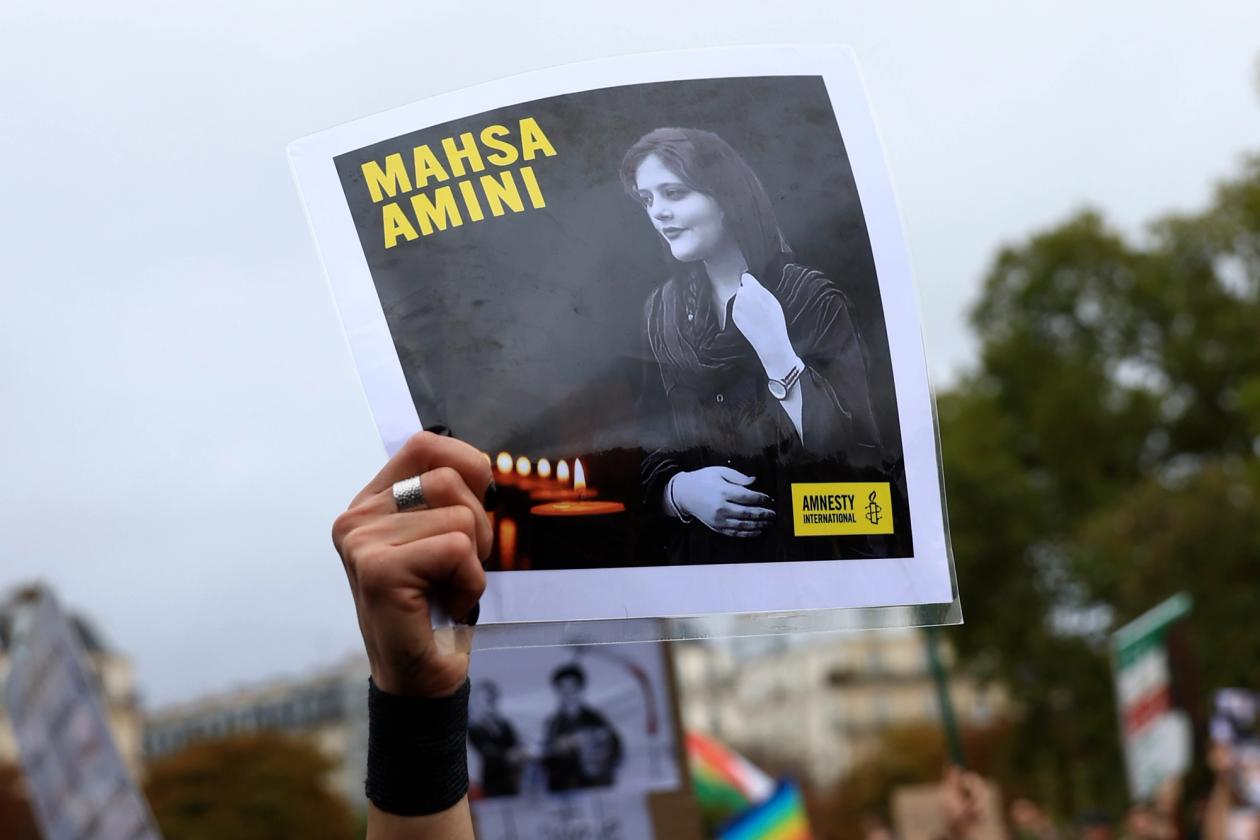 En plakat i et demonstrasjonstog. På plakaten er det et svart-hvitt bilde av en ung iransk kvinne, med navnet MASHA AMINLI i gule bokstaver oppe til venstre og Amnesty International sin logo nederst til høyre.