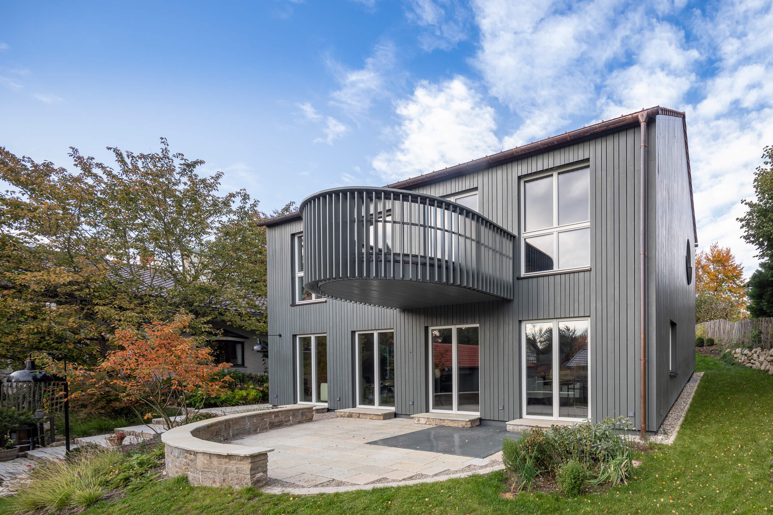 Goetz Castorph Lehmann Tabillion Architektur Städtebau München Holzbau grau Fenster rund Einfamilienhaus Balkon auskragend Haus im Haus Holzschalung Schalungsbretter unterschiedliche Breiten