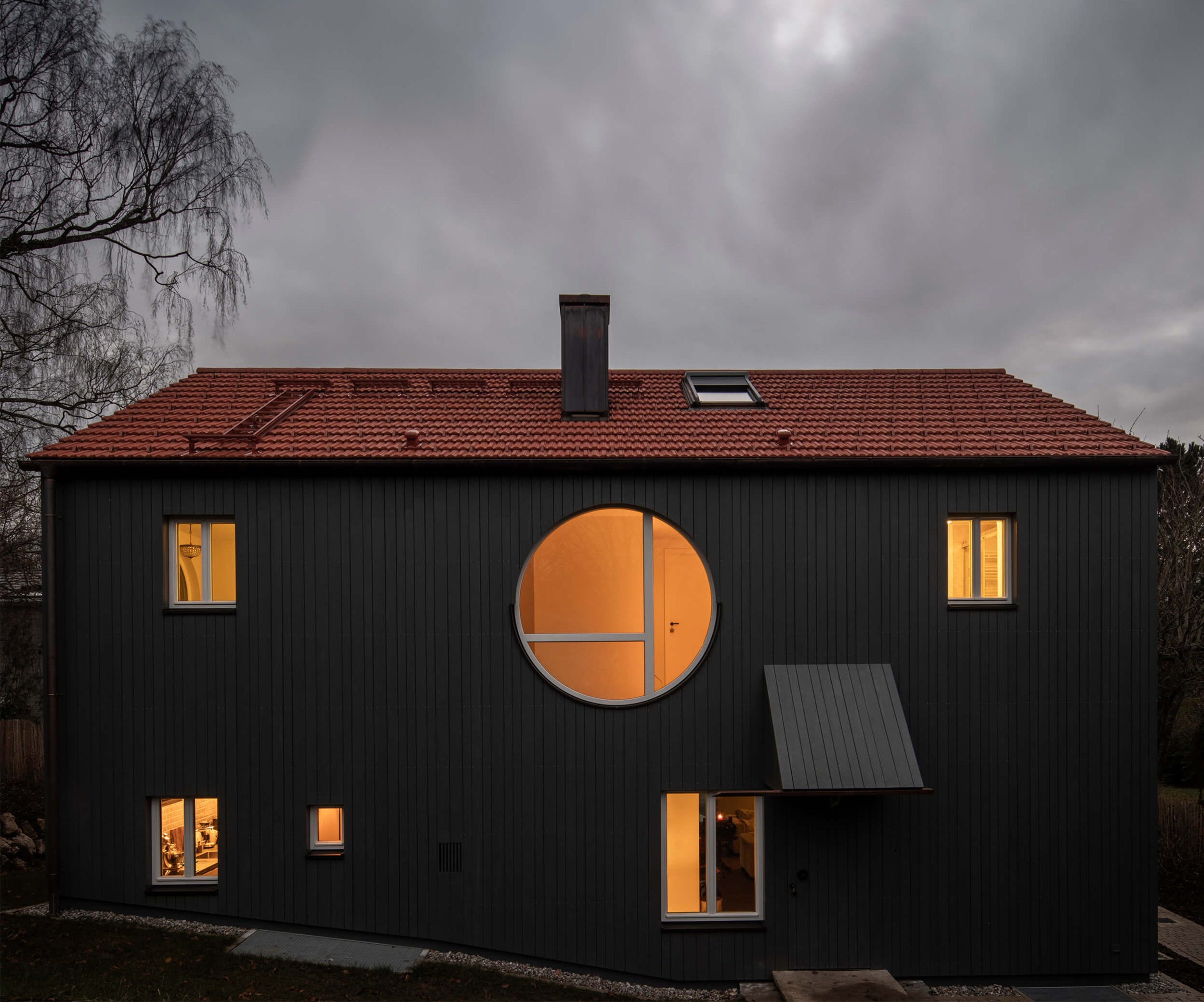 Goetz Castorph Lehmann Tabillion Architektur Städtebau München Holzbau grau Fenster rund Einfamilienhaus Balkon auskragend Haus im Haus Holzschalung Schalungsbretter unterschiedliche Breiten Nacht