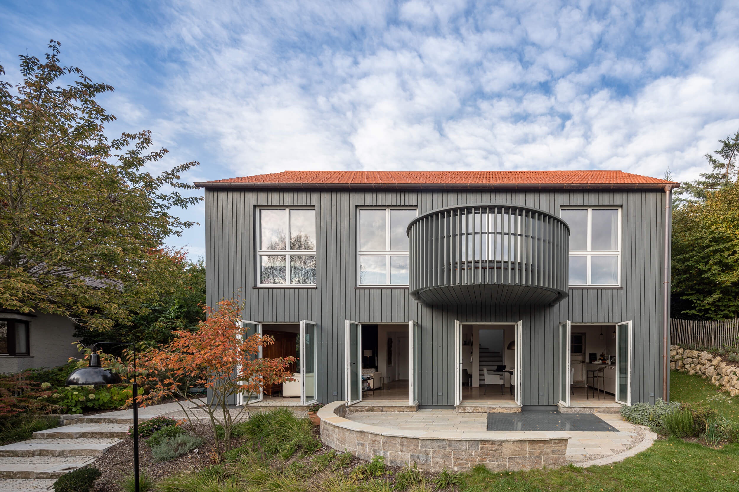 Goetz Castorph Lehmann Tabillion Architektur Städtebau München Holzbau grau Fenster rund Einfamilienhaus Balkon auskragend Haus im Haus Holzschalung Schalungsbretter unterschiedliche Breiten