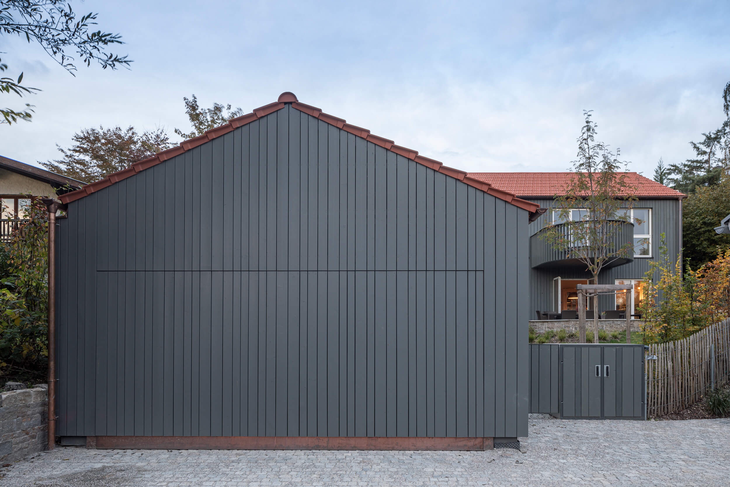 Goetz Castorph Lehmann Tabillion Architektur Städtebau München Holzbau grau Fenster rund Einfamilienhaus Balkon auskragend Haus im Haus Holzschalung Schalungsbretter unterschiedliche Breiten Garage