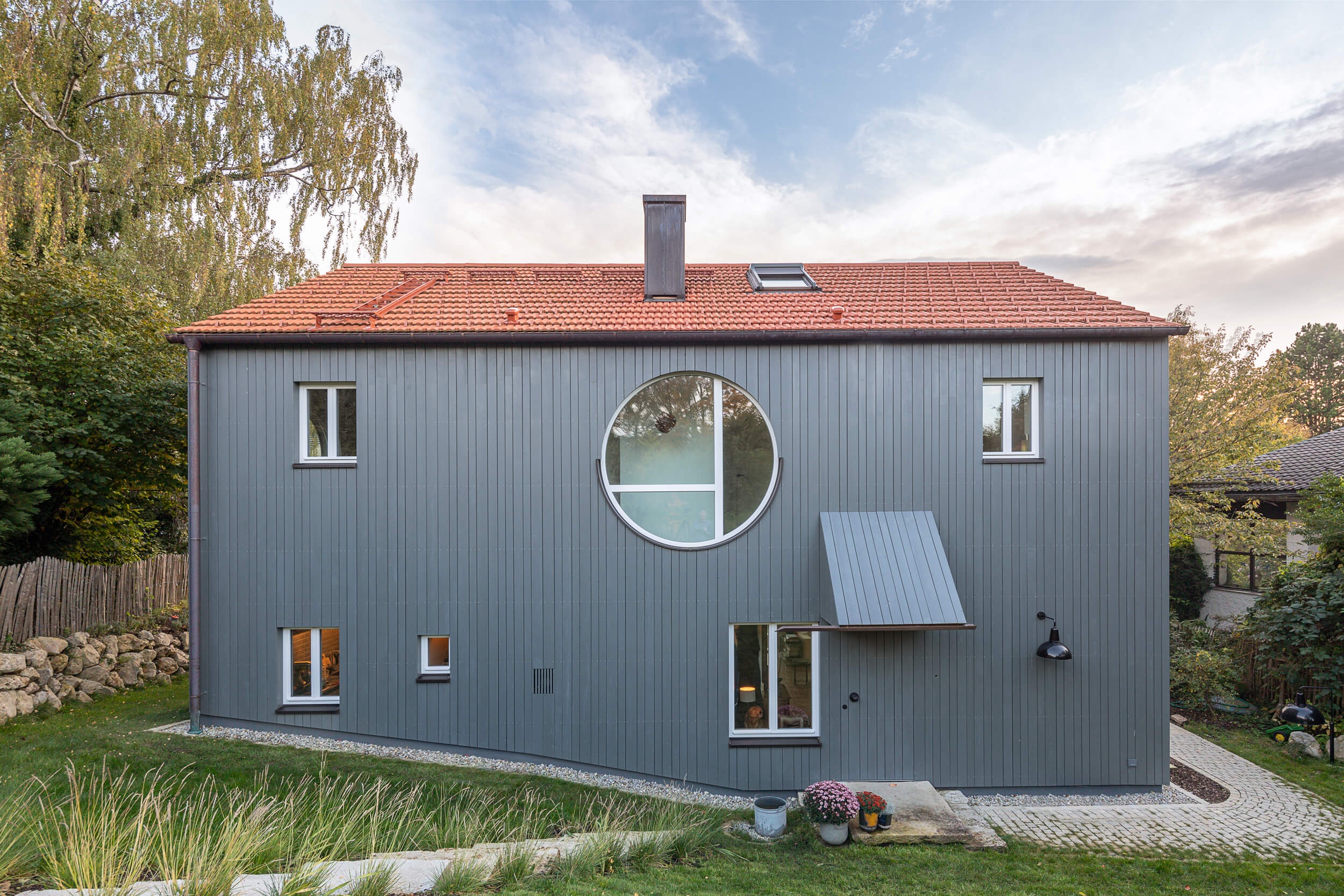 Goetz Castorph Lehmann Tabillion Architektur Städtebau München Holzbau grau Fenster rund Einfamilienhaus Balkon auskragend Haus im Haus Holzschalung Schalungsbretter unterschiedliche Breiten