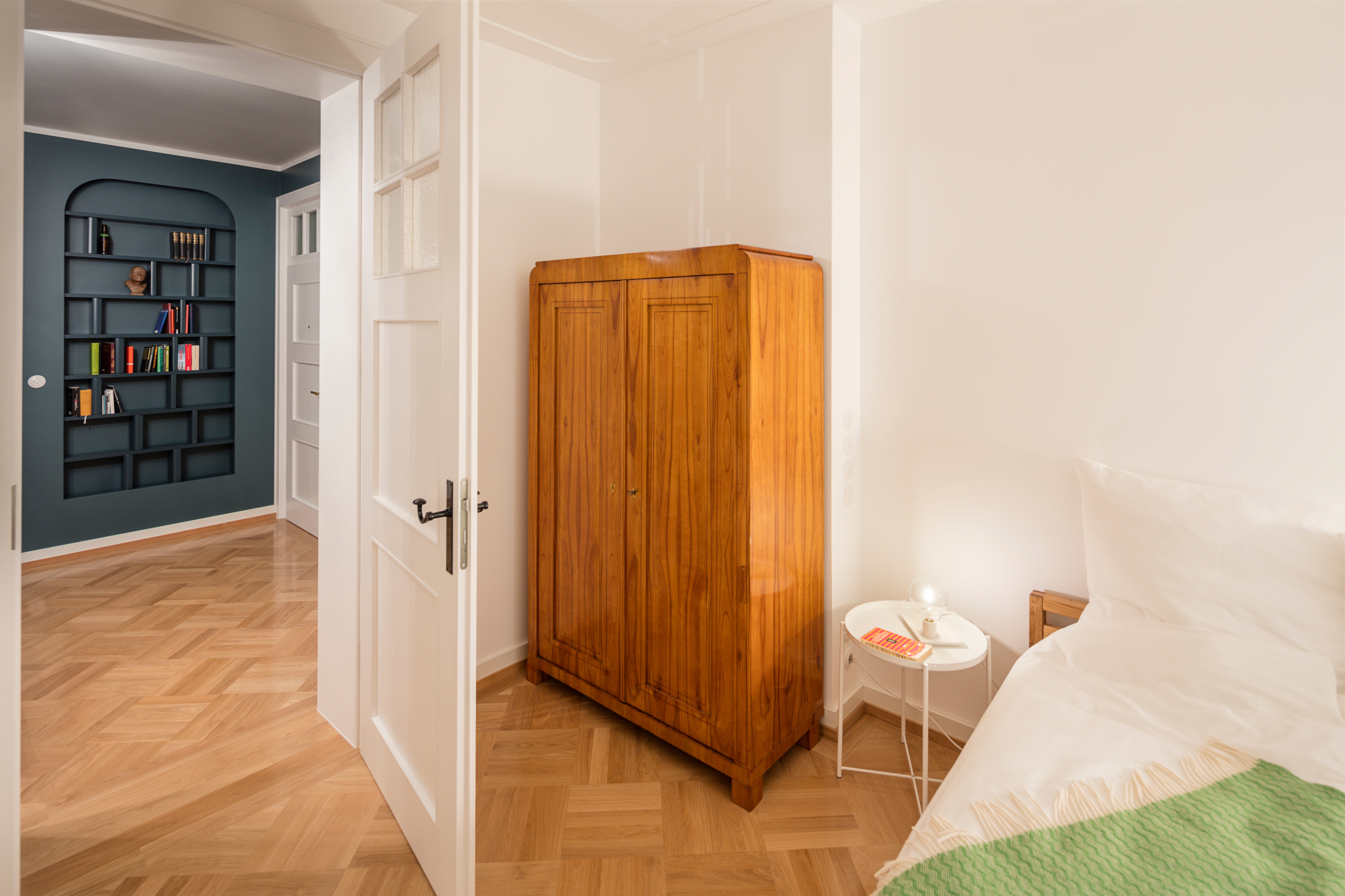 Betrachtet man die Baustellenbilder, wird klar, dass nichts von dem, was heute auf den ersten Blick so selbstverständlich erscheint, vor dem Umbau vorhanden war – nicht das Eichenholzparkett mit seinem klassisch schönen Speckglanz; nicht die vielen praktischen, kleinen und großen Wandnischen; nicht die sanften Stuckaturen der Zimmerdecken und auch nicht die gegliederten Türen ... Wo früher ein Unterzug und Kaminvorsprünge den Raum willkürlich beherrschten, zonieren nun räumliche Einbauten die Wohnung und formen Beziehungen – wie z.B. die Nische am Essplatz zur Tischform – und zum Siebdruck Rupprecht Geigers. Die spielerische Wiederaneignung bekannter und vielfach bewährter Elemente verleiht der Wohnung ihren zeitlosen wie heiteren Charakter.