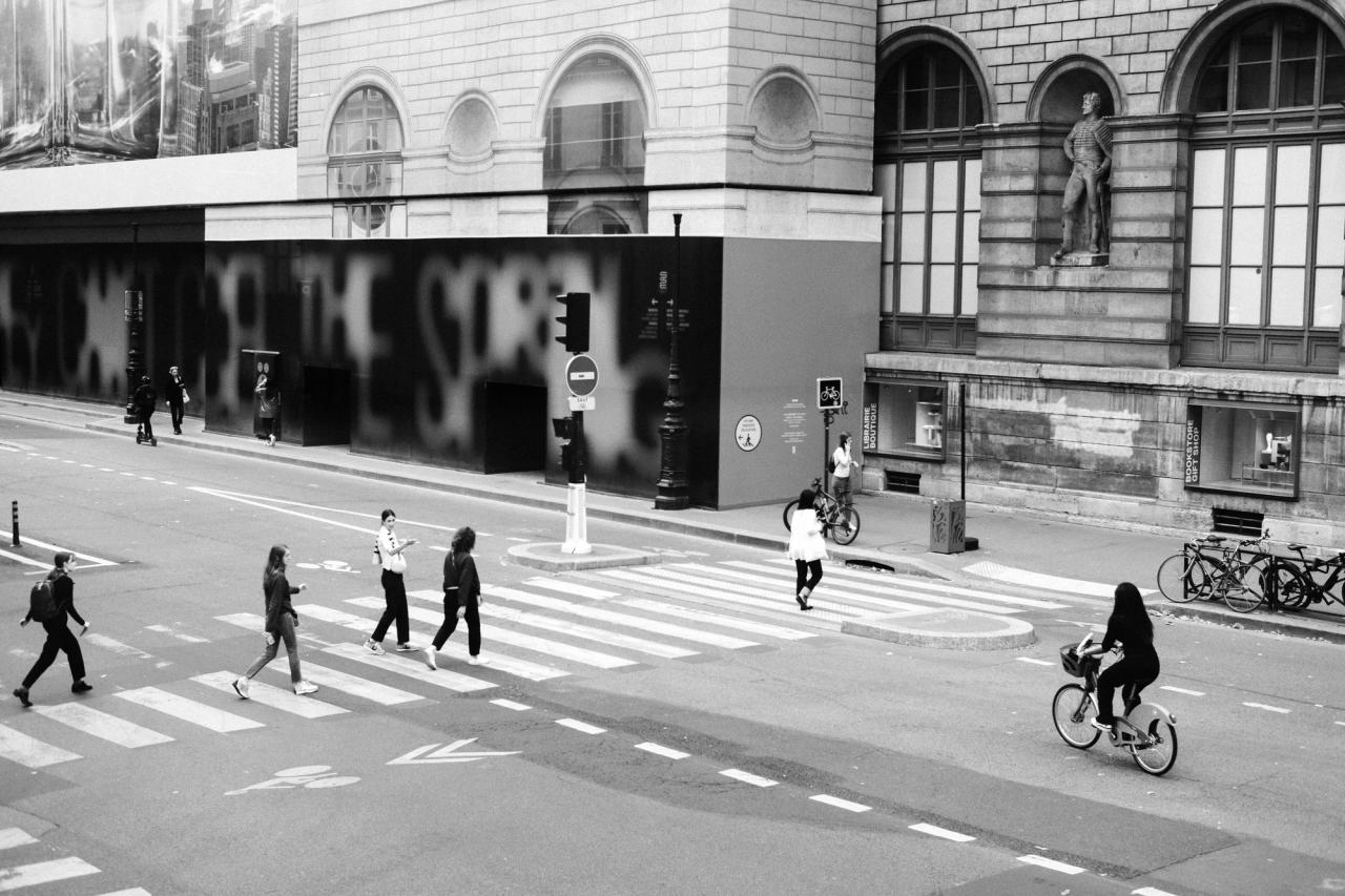 Pedestrians and a cyclist at a marked crosswalk on a city street.