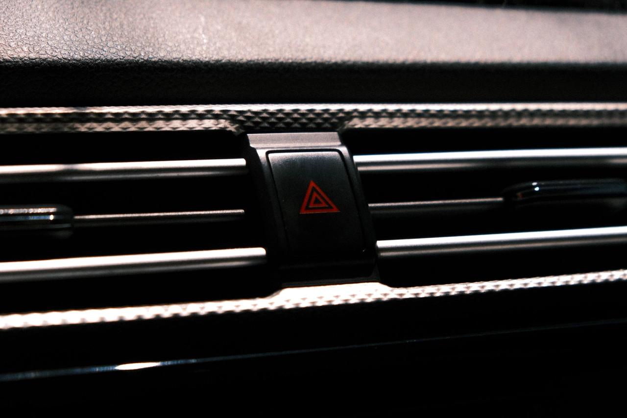 A hazard light button on a dark car dashboard.