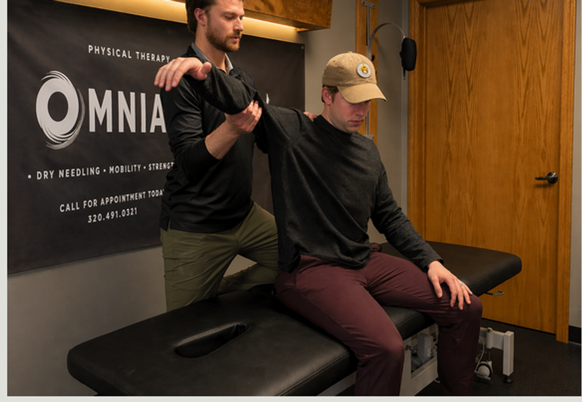 Therapist guiding a seated overhead shoulder stretch