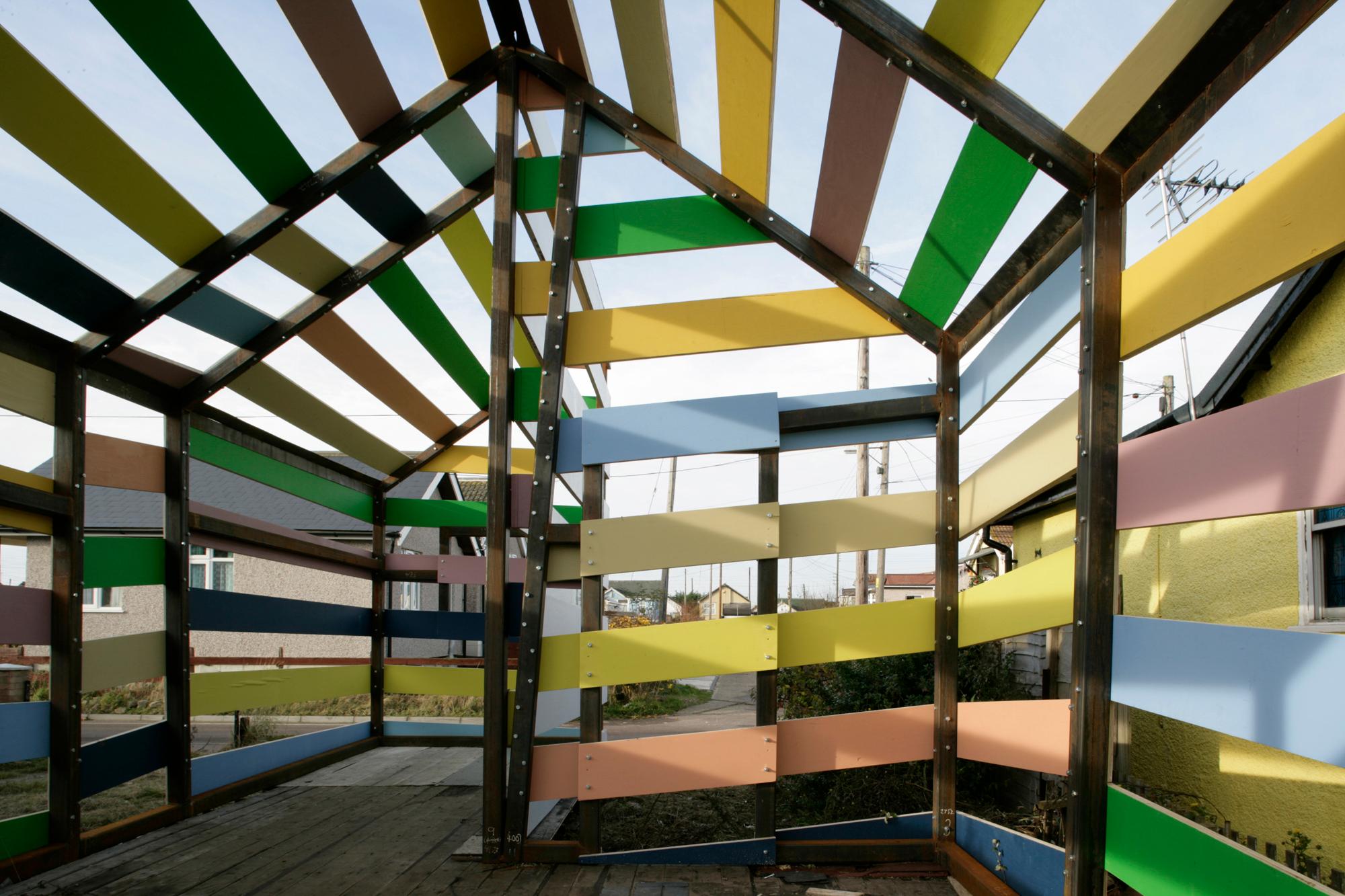 An open, house-shaped structure with a dark frame and horizontal slats in various bright colors.