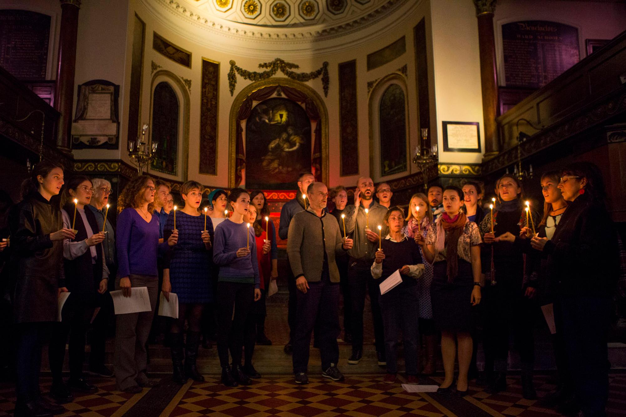 A choir sings, holding lit candles, in a dimly lit church.