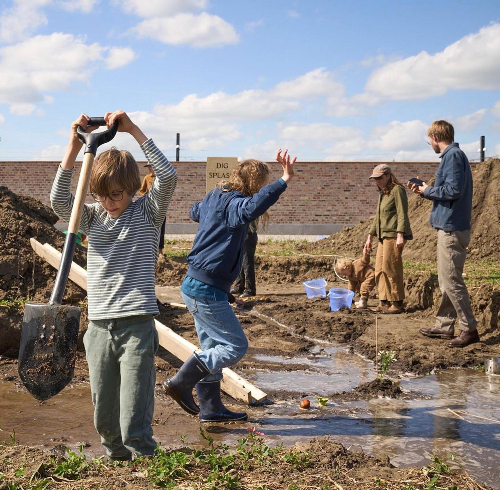 Children and adults playing in a muddy, watery outdoor area with shovels.