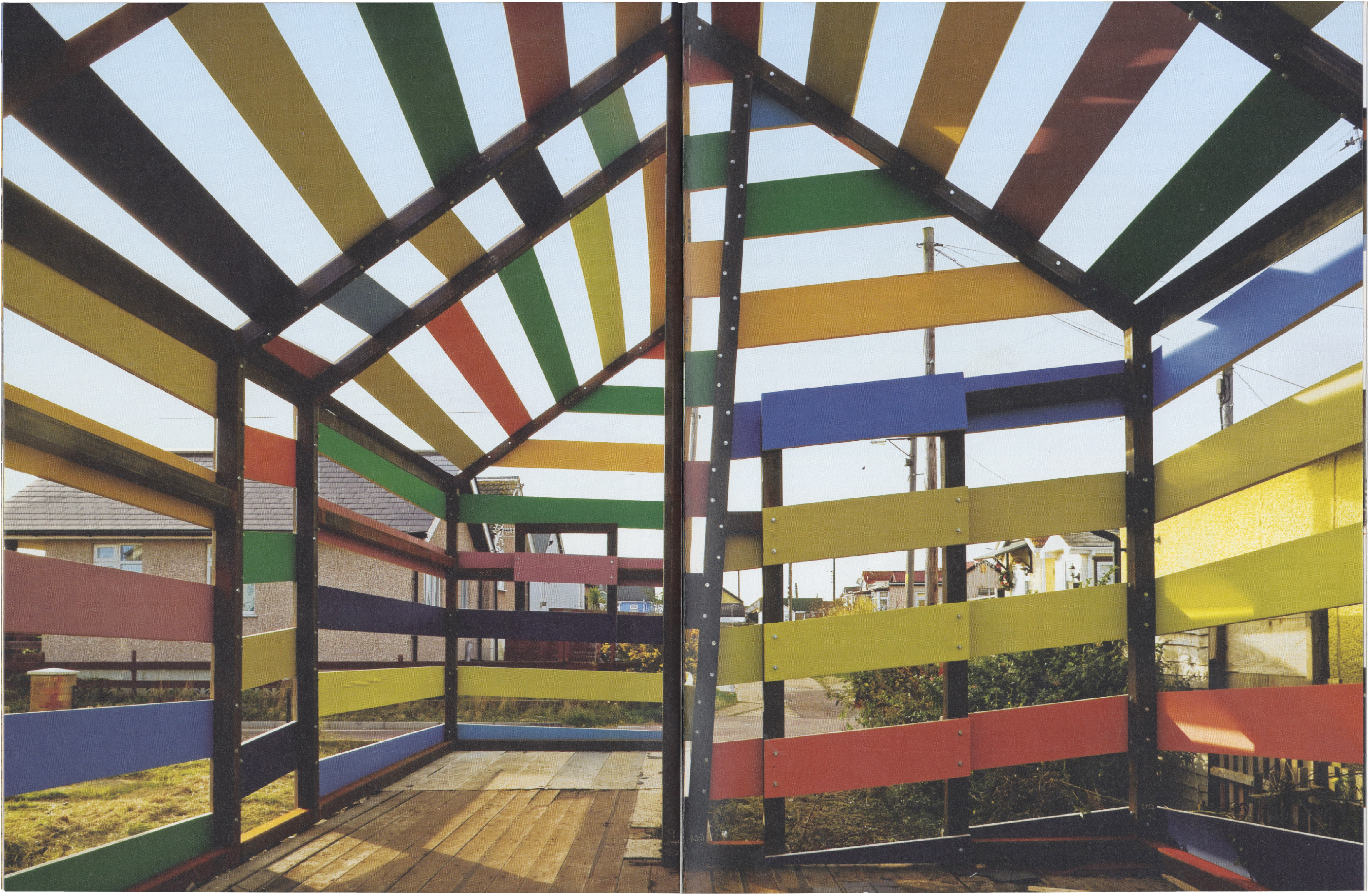 Colorful open-sided A-frame structure with horizontal slats, overlooking a suburban scene.