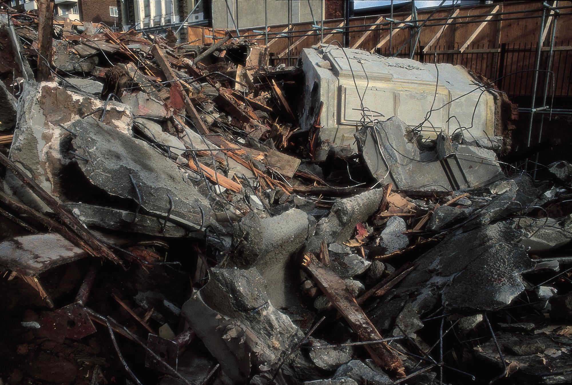 A dense pile of concrete rubble, twisted rebar, and wooden debris from a demolished building.