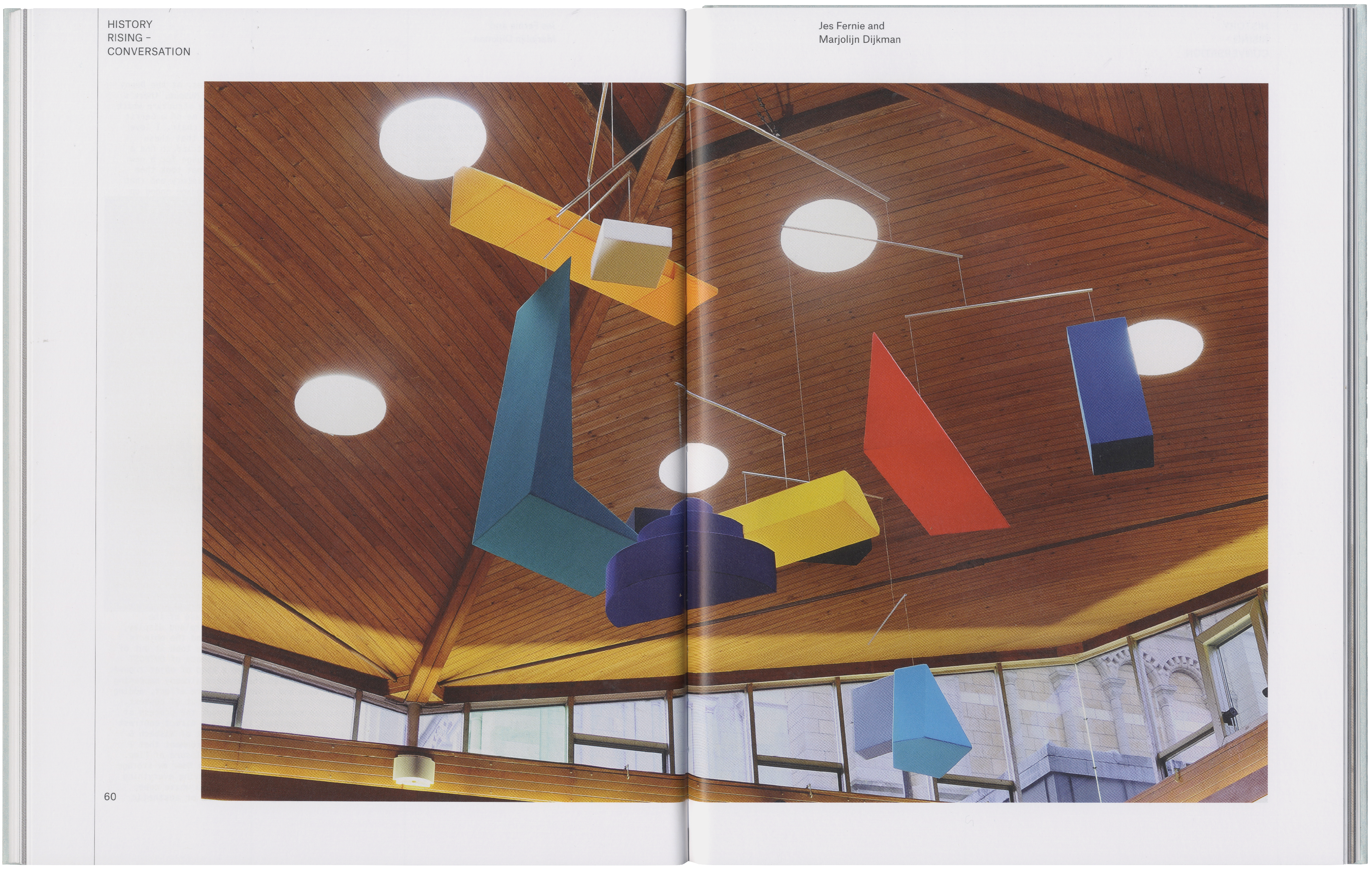 A large, colorful geometric mobile hangs from a vaulted wooden ceiling with circular lights.