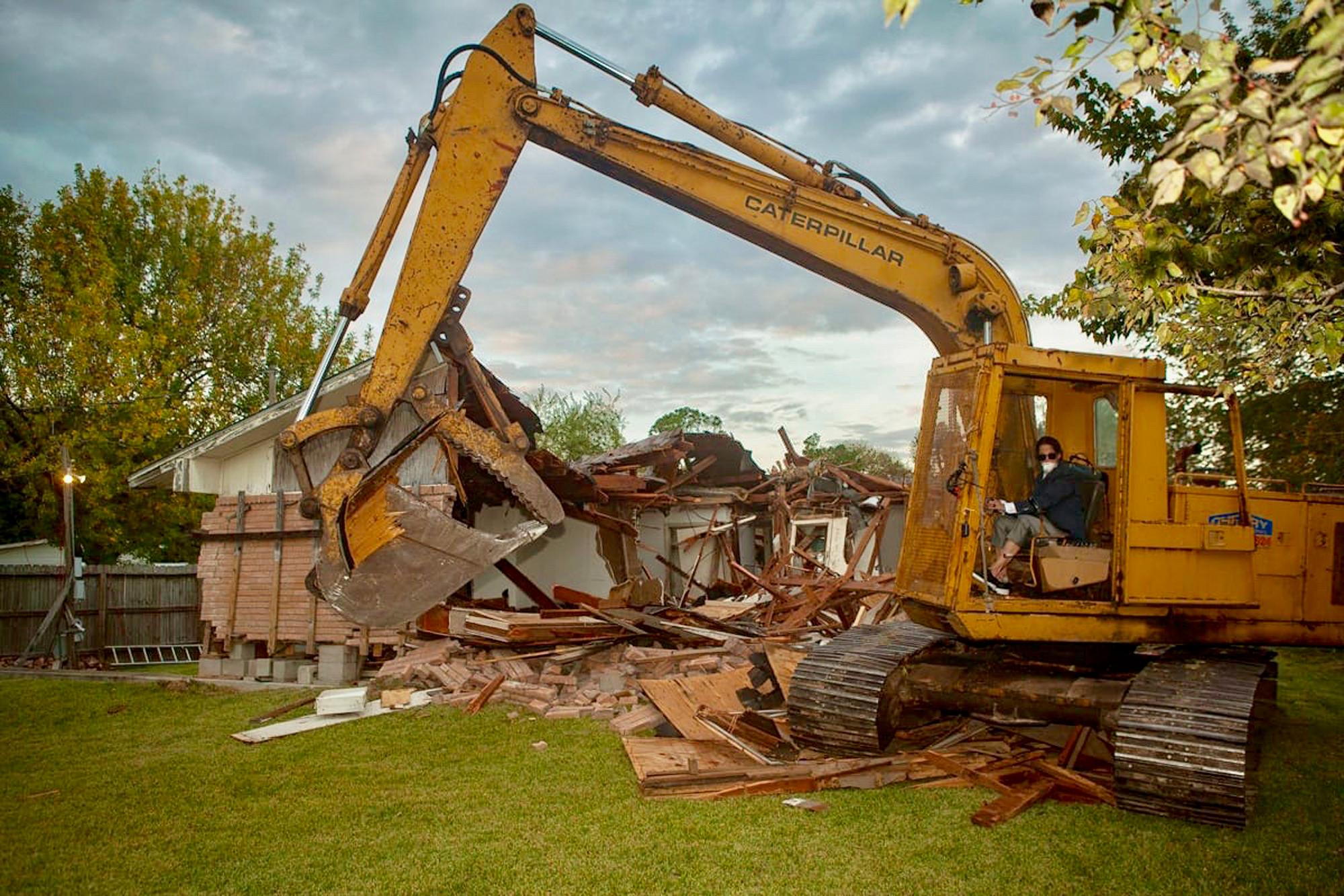 A person in a yellow excavator demolishing a house.