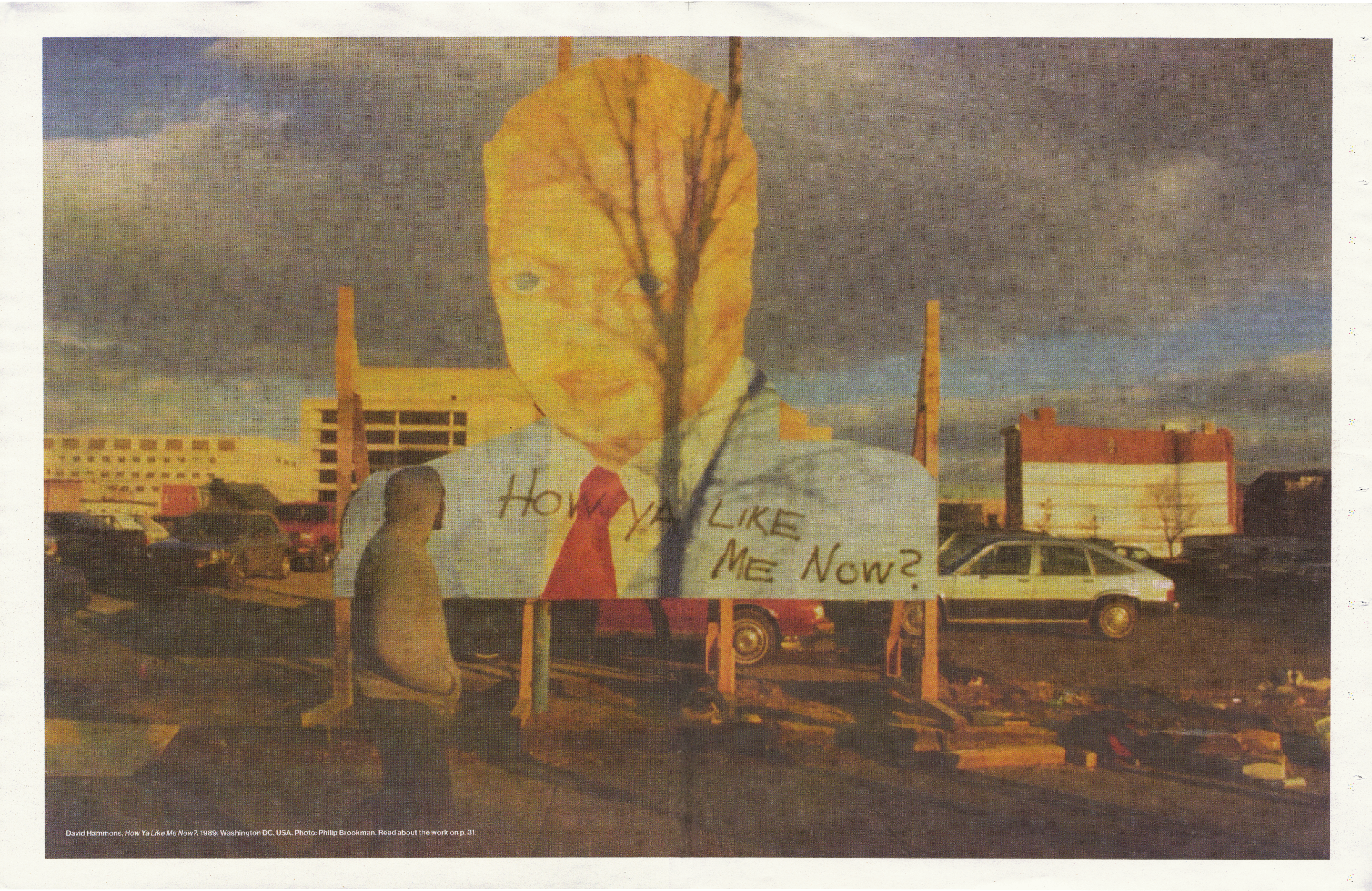 A large outdoor cutout of a man's head and torso, with a tree branch across his face, wearing a blue shirt and red tie, above a sign that reads 'How ya like me now?'.