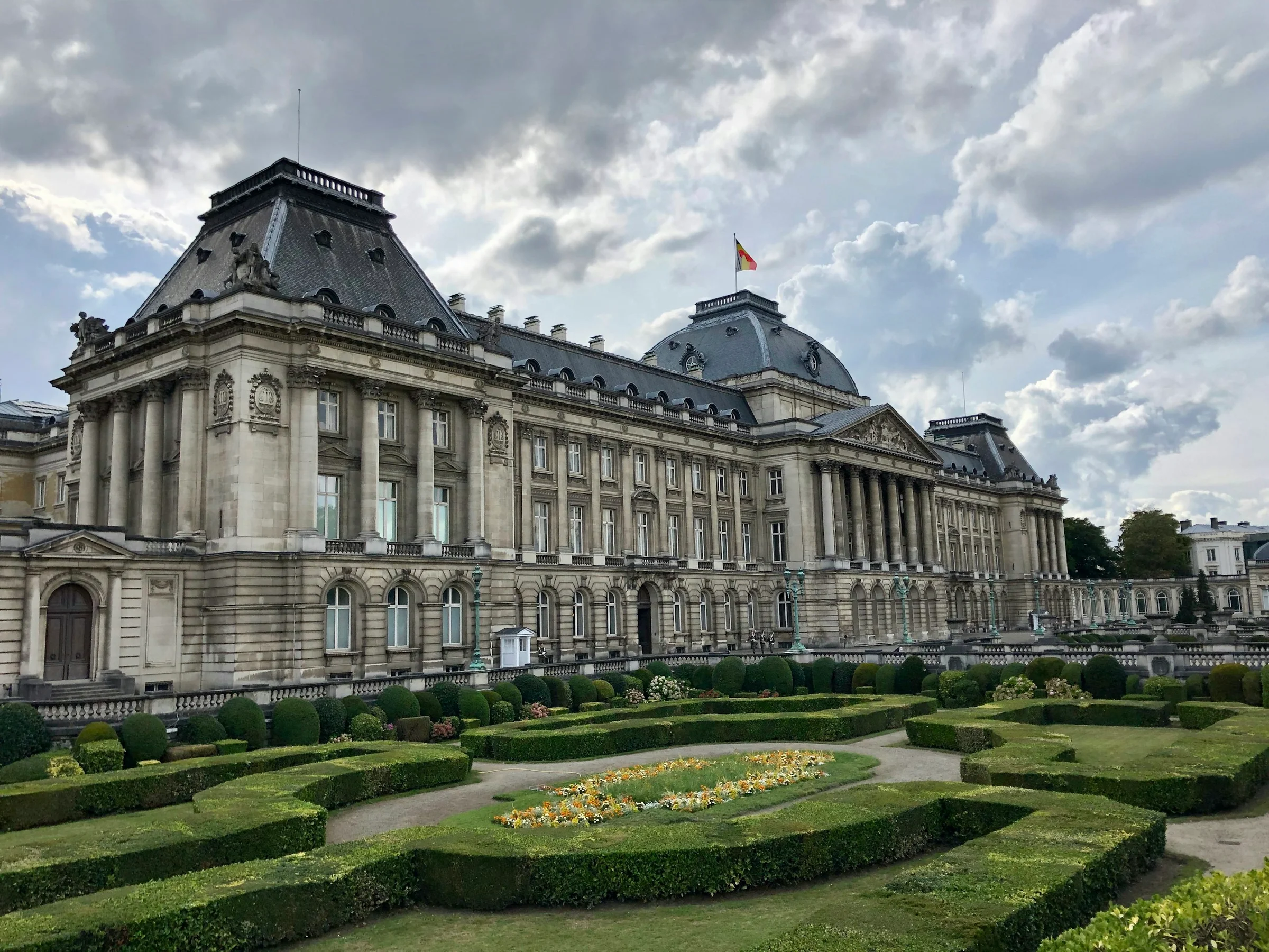 Royal Palace Brussels dan taman berpagar rapi di bawah langit berawan.