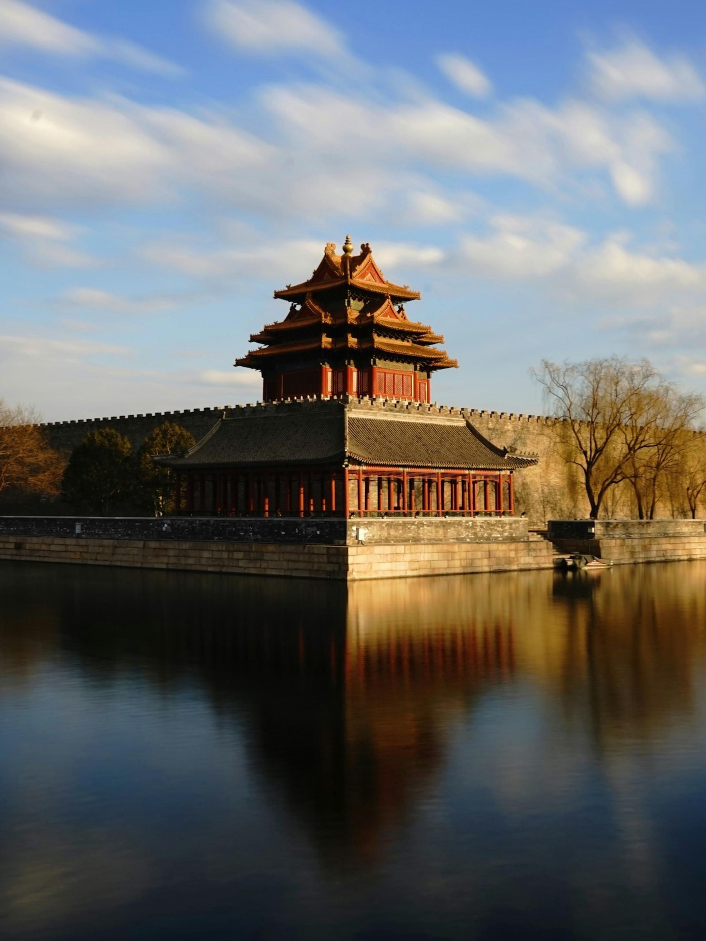 Menara sudut Kota Terlarang Beijing dengan refleksi di parit, cahaya keemasan.
