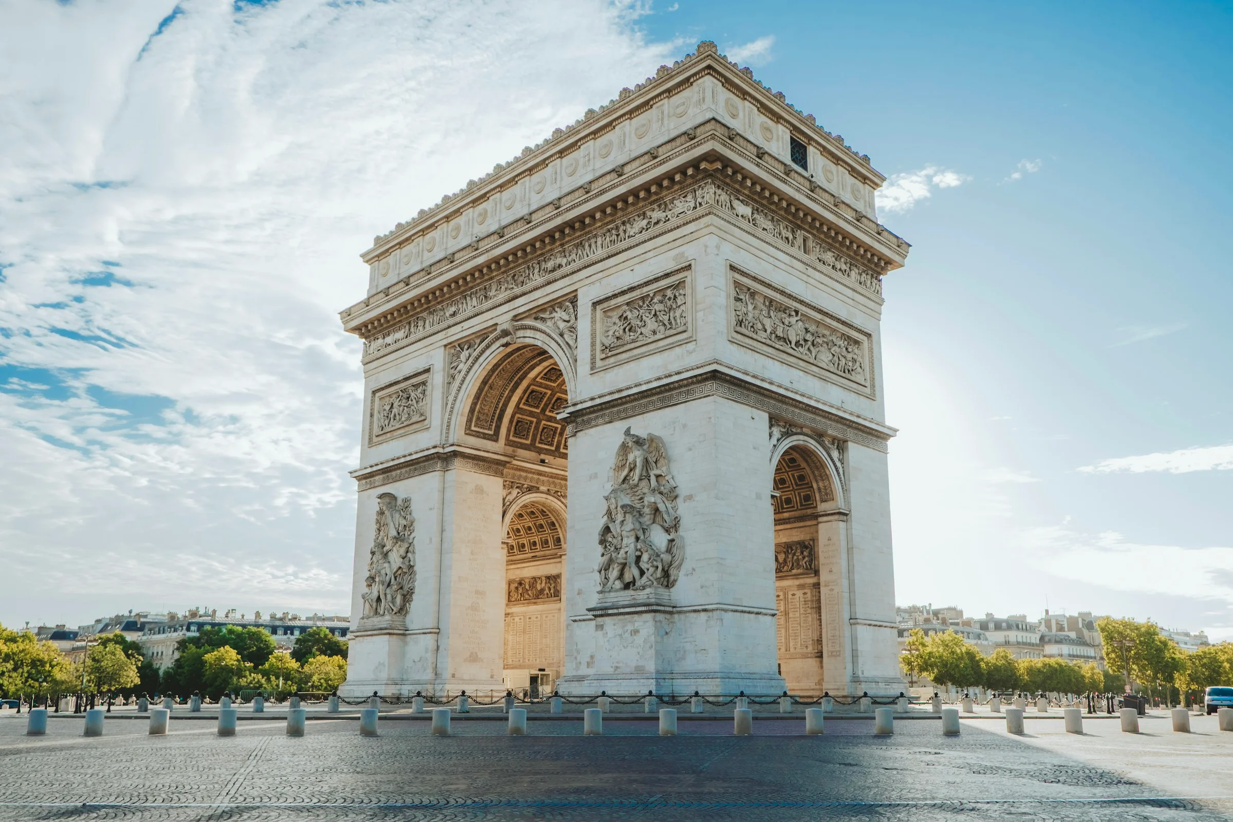 Arc de Triomphe di Paris dari sudut rendah dengan langit biru dan awan tipis.