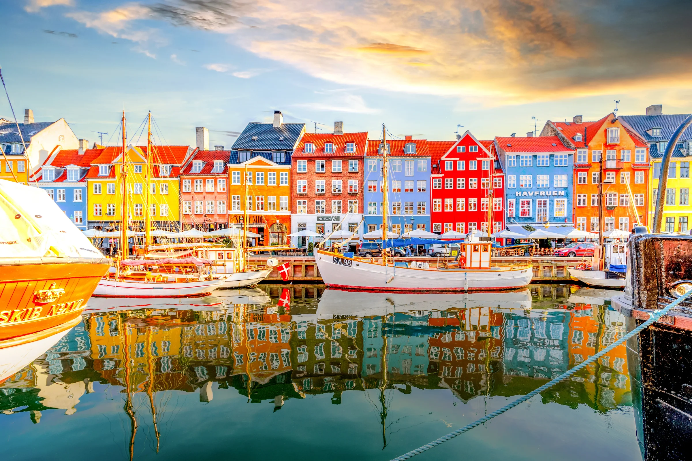 Tepi air Nyhavn Copenhagen menjelang sore dengan perahu kayu dan pantulan warna di kanal