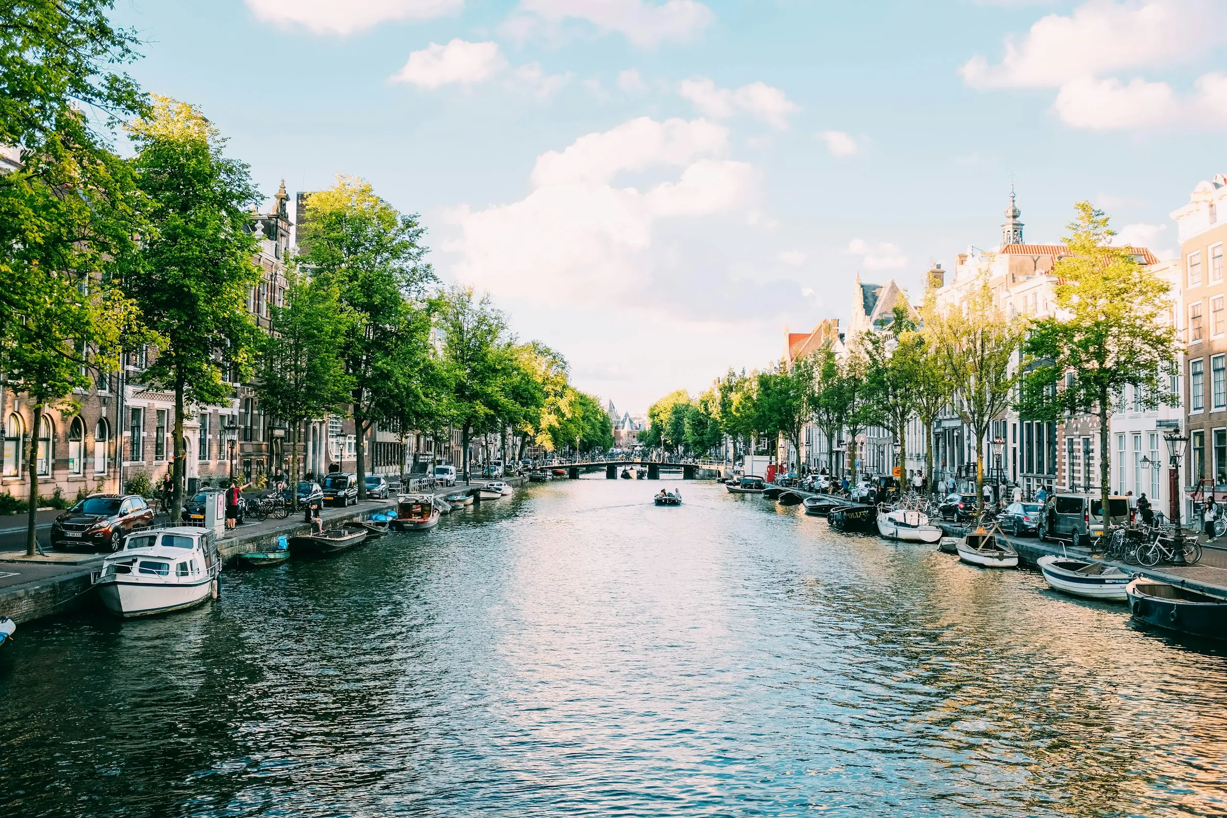 Kanal Amsterdam dikelilingi pepohonan hijau dan deretan rumah klasik Belanda
